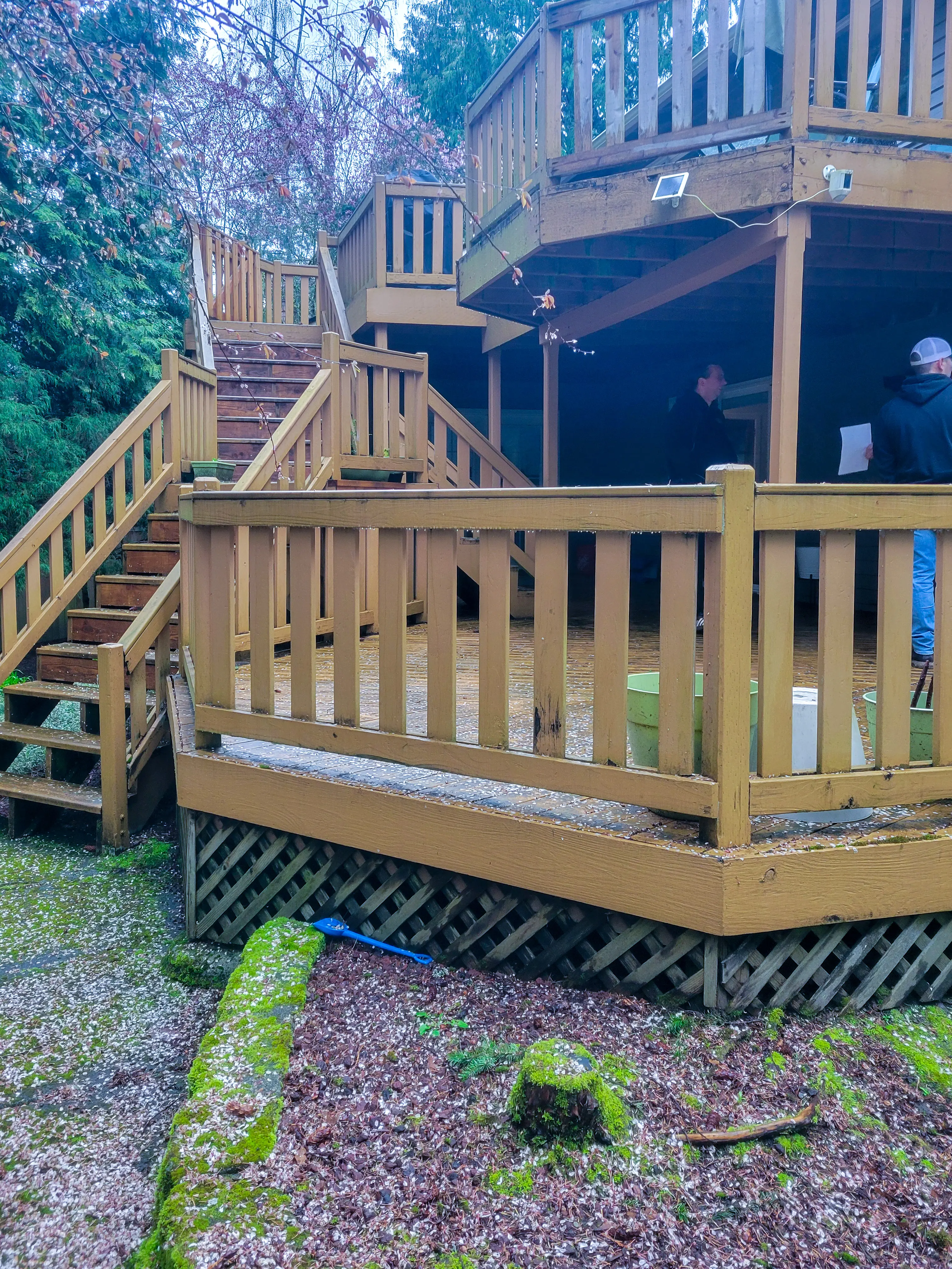 Existing multi-level wood deck and stairs behind a Kirkland, WA home, with two people standing on the lower deck before construction began.