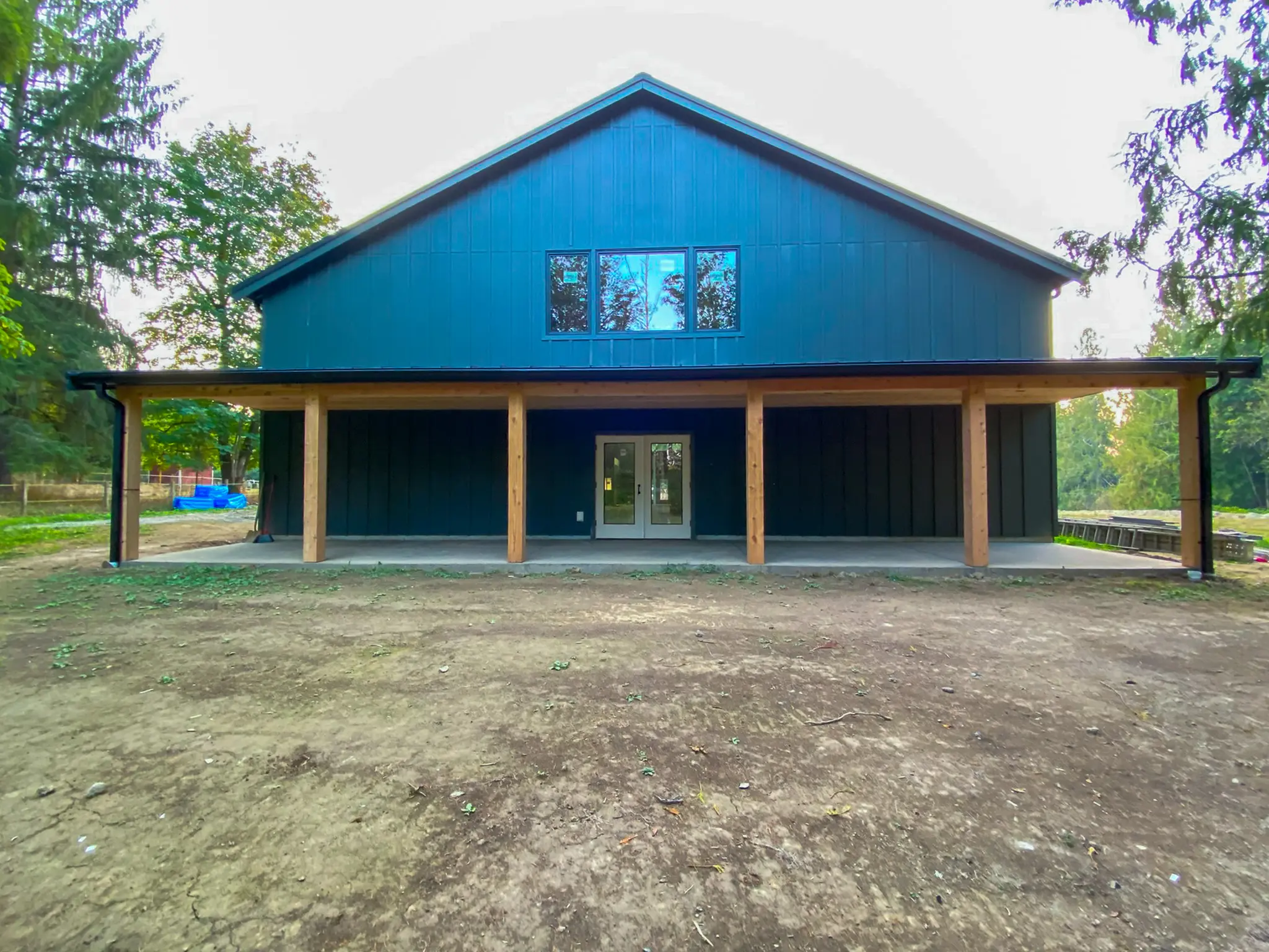 Front elevation of the completed detached shop in Fall City, WA, showing its covered porch, timber posts, and paired entry doors.