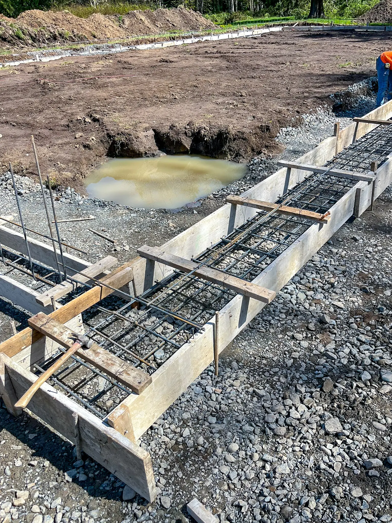 Concrete foundation forms with rebar and gravel base under construction for a Fall City, WA whole-home remodel and addition, with a worker on site.