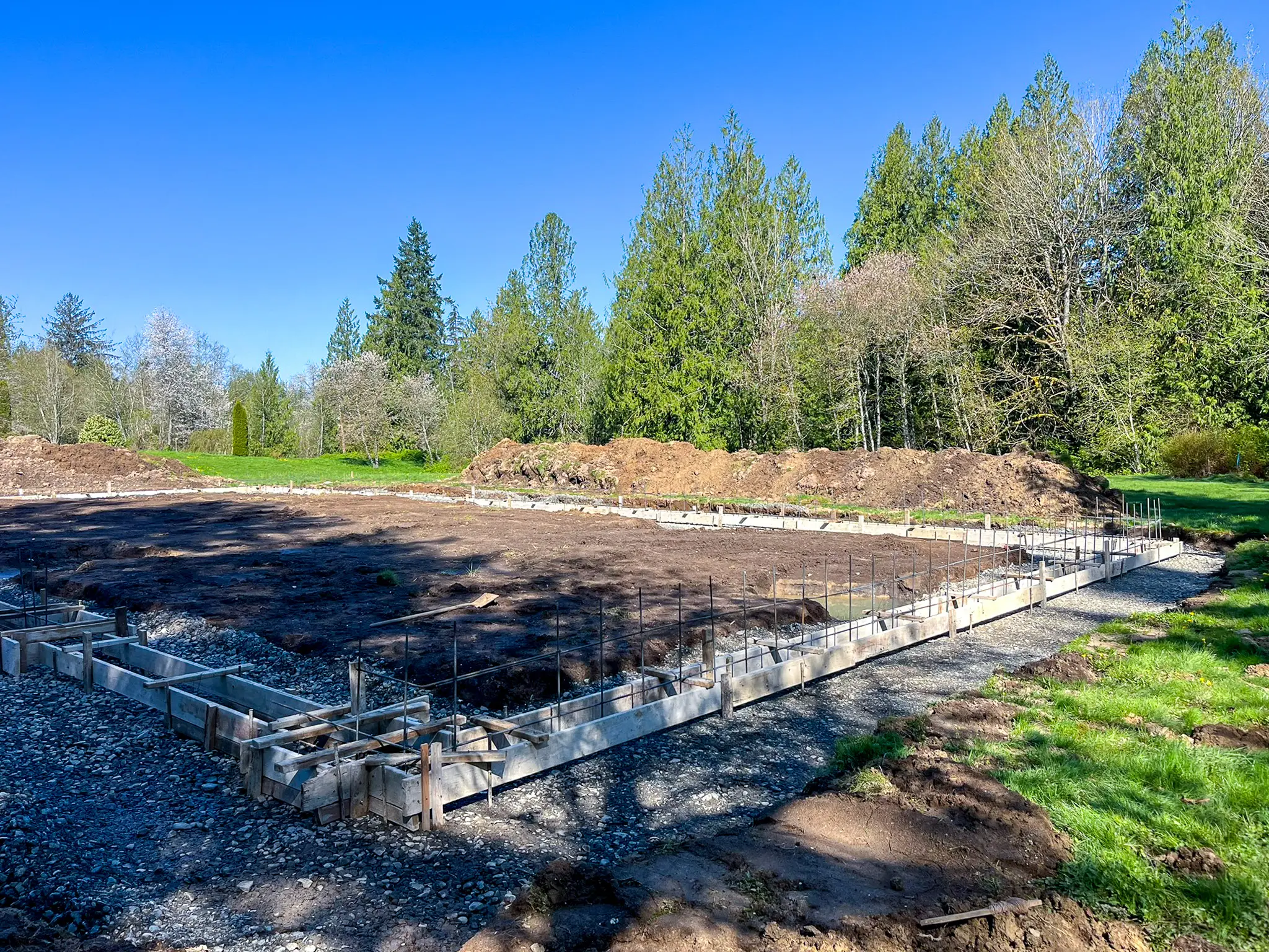 Wide view of foundation footing trenches outlining a building footprint on a wooded Fall City, WA property before a whole-home remodel and addition.
