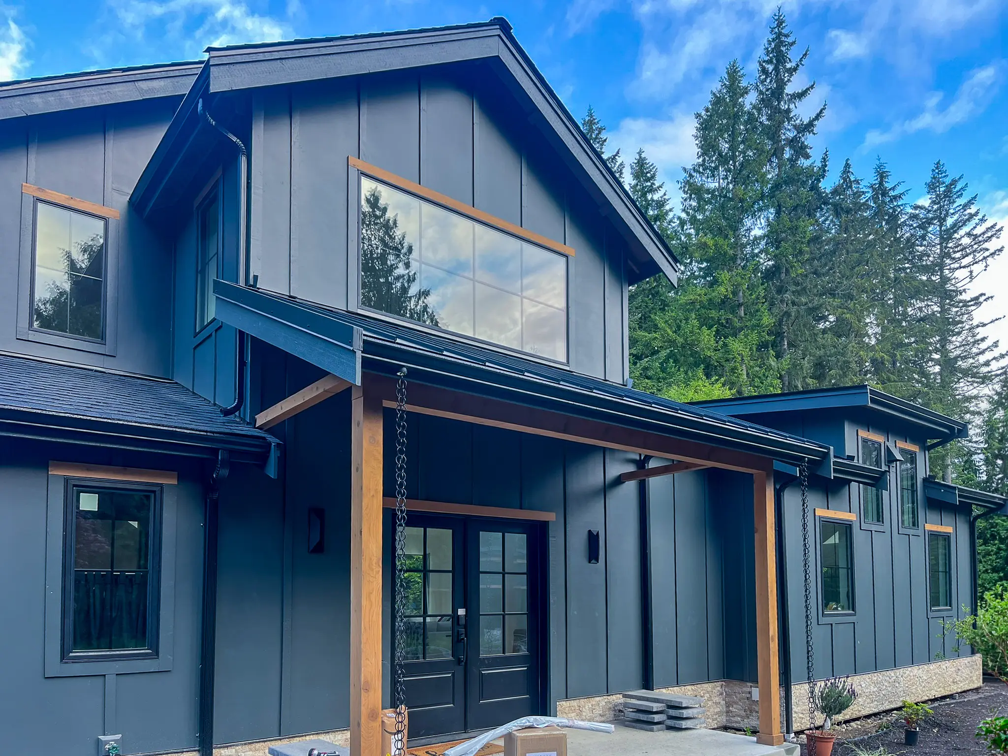 Covered front entry of a new custom home in Redmond, WA, with wood posts, glass double doors, and a large upper window.