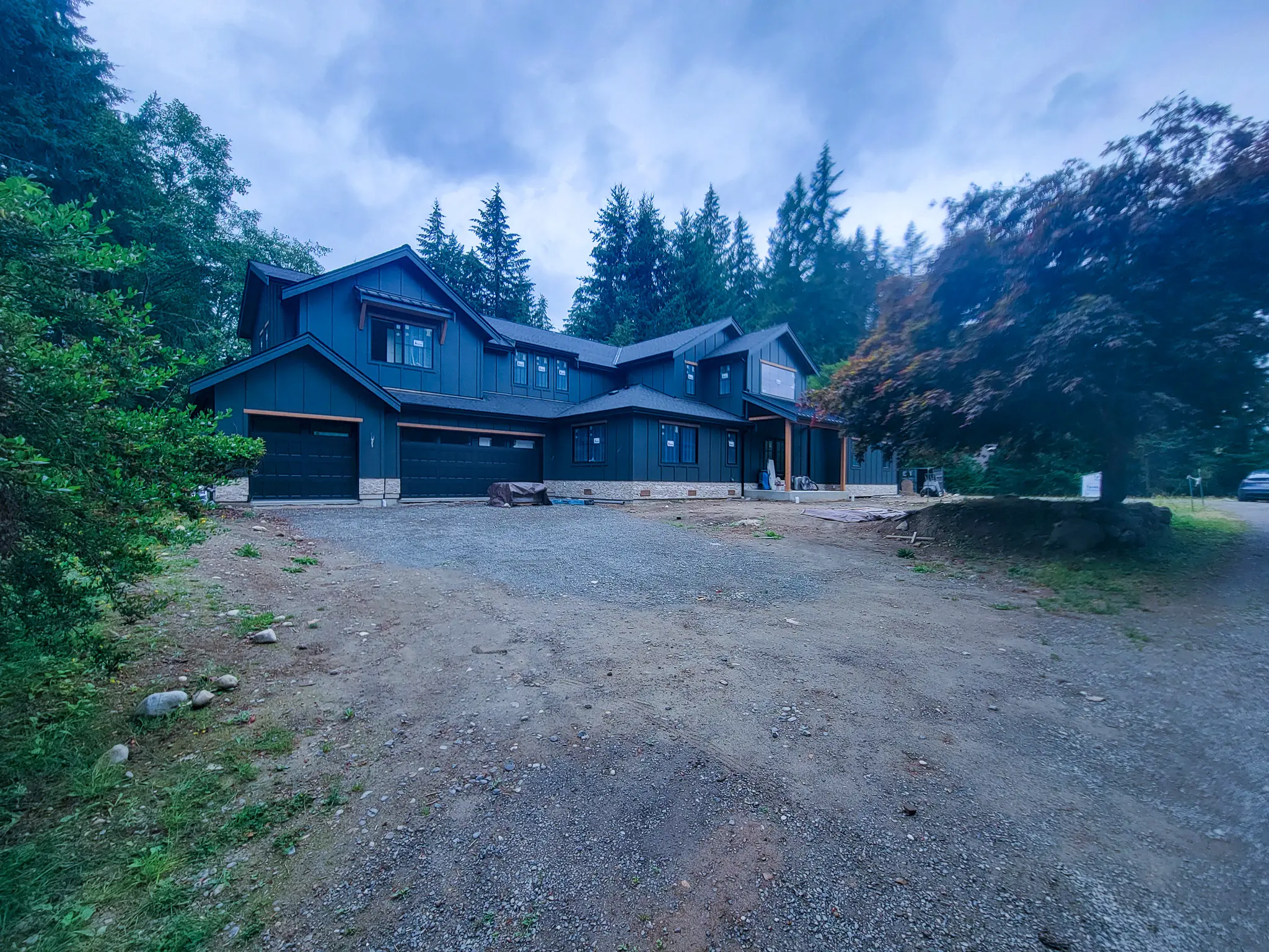 Full facade of a new custom home in Redmond, WA, at dusk, with dark board-and-batten siding and multiple gables.