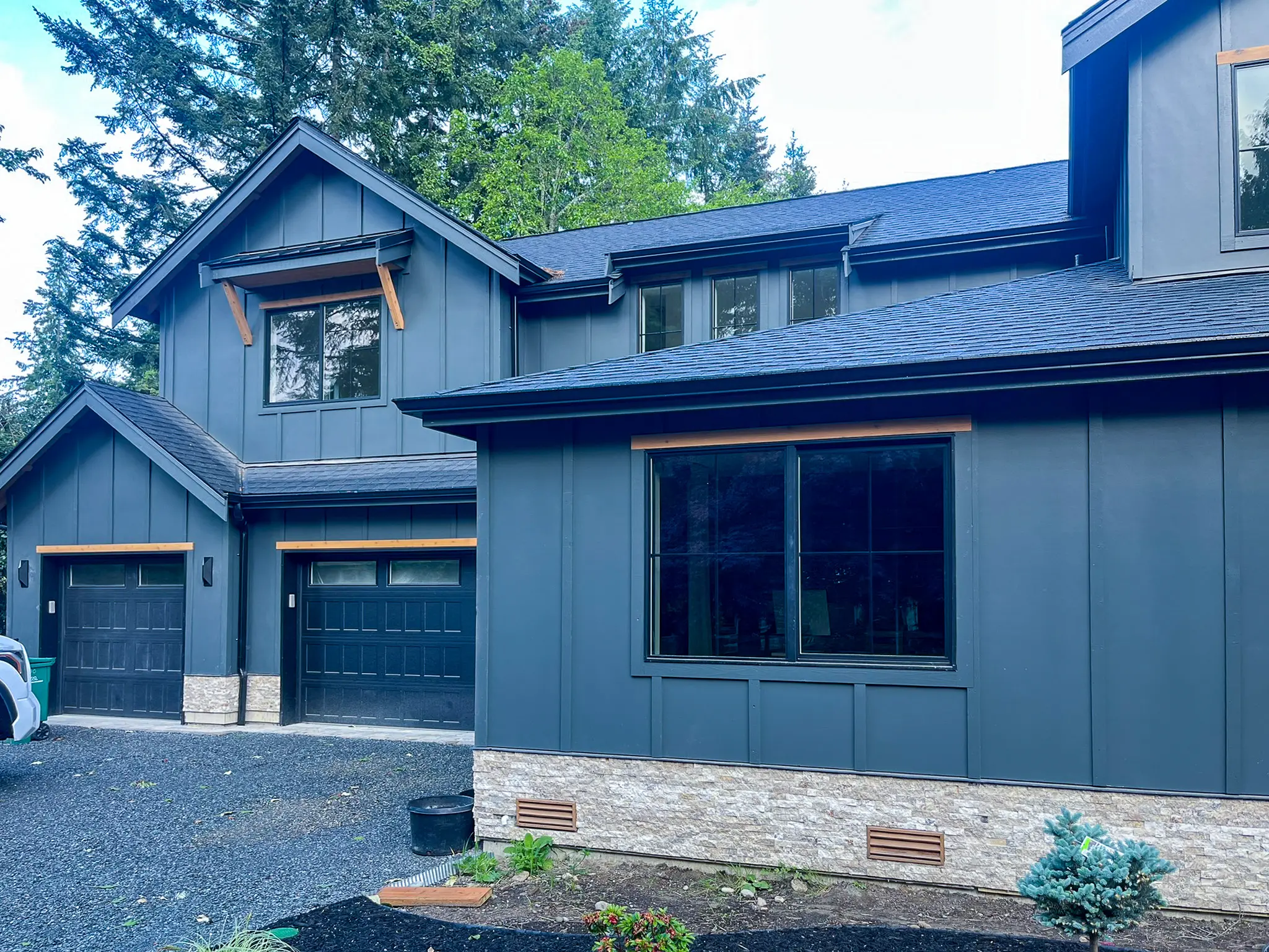 Angled exterior view of a new custom home in Redmond, WA, showing dark siding, a stone accent base, and two garage doors.