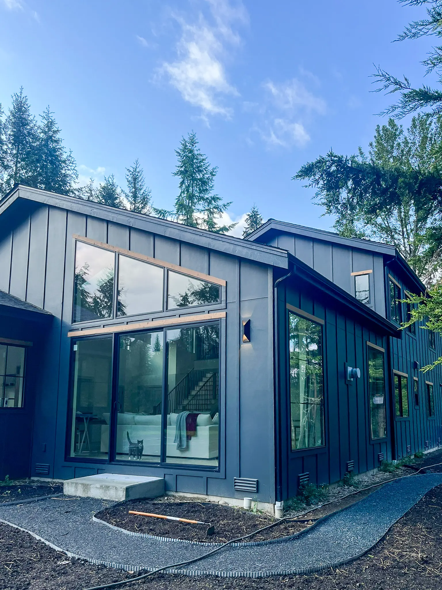 Rear exterior corner of a new custom home in Redmond, WA, with a tall window wall looking into a staircase and living area.