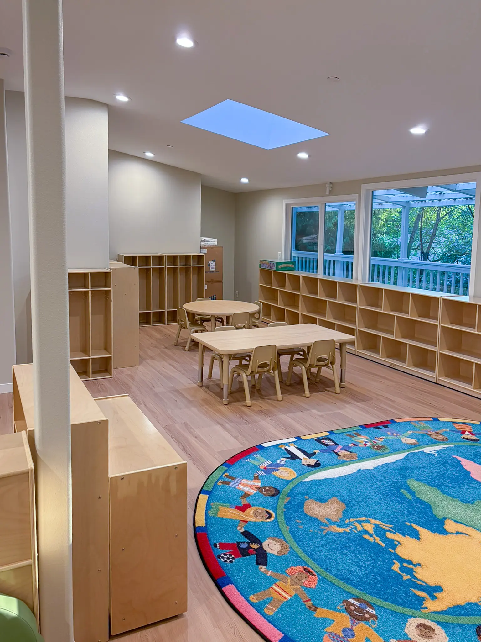 Classroom with a skylight, low storage cubbies, children's tables and chairs, and a round rug in the remodeled Redmond, WA daycare.