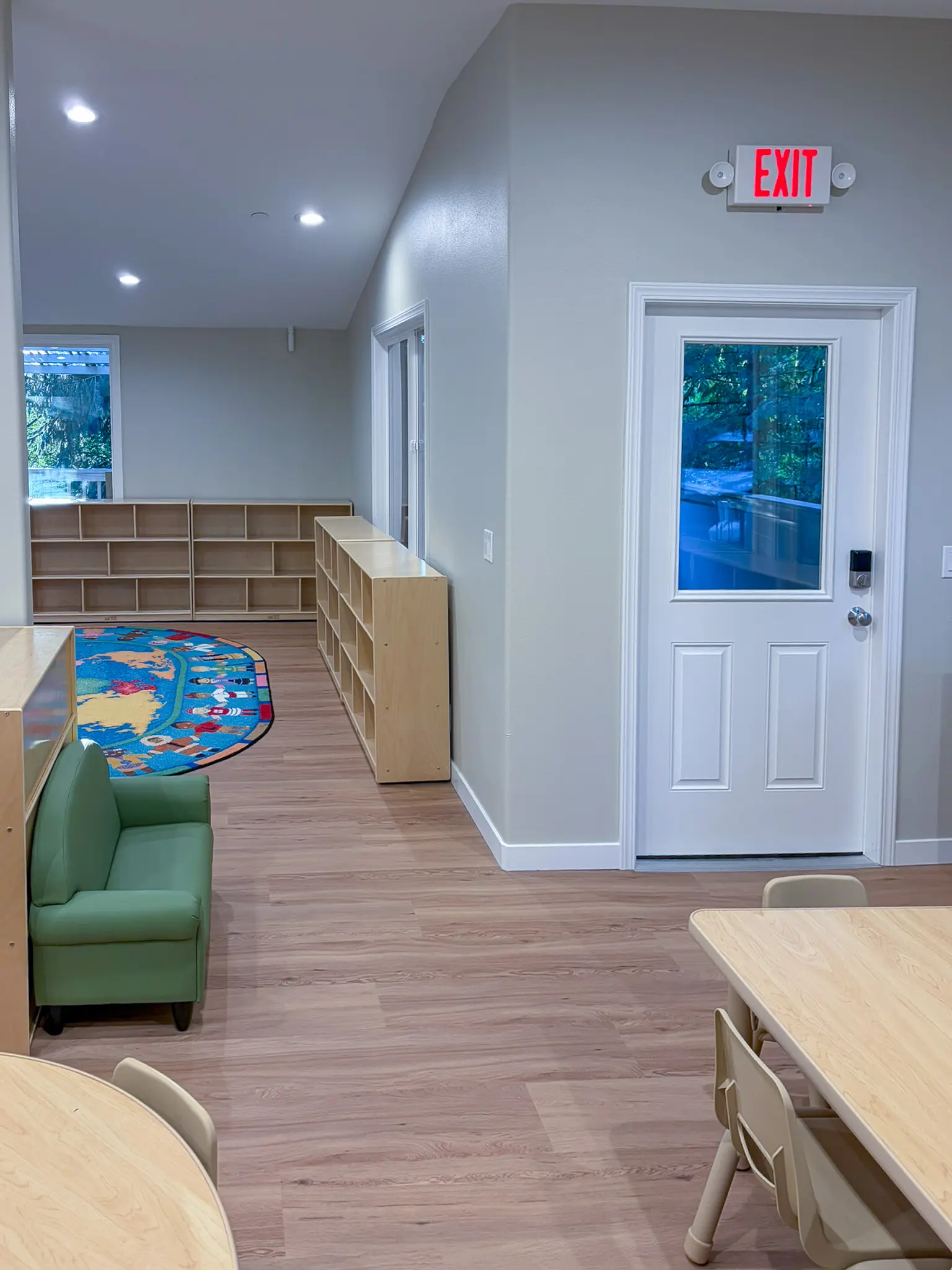 Classroom seating area with a small sofa, a round rug, and an exit door in the remodeled Redmond, WA daycare.