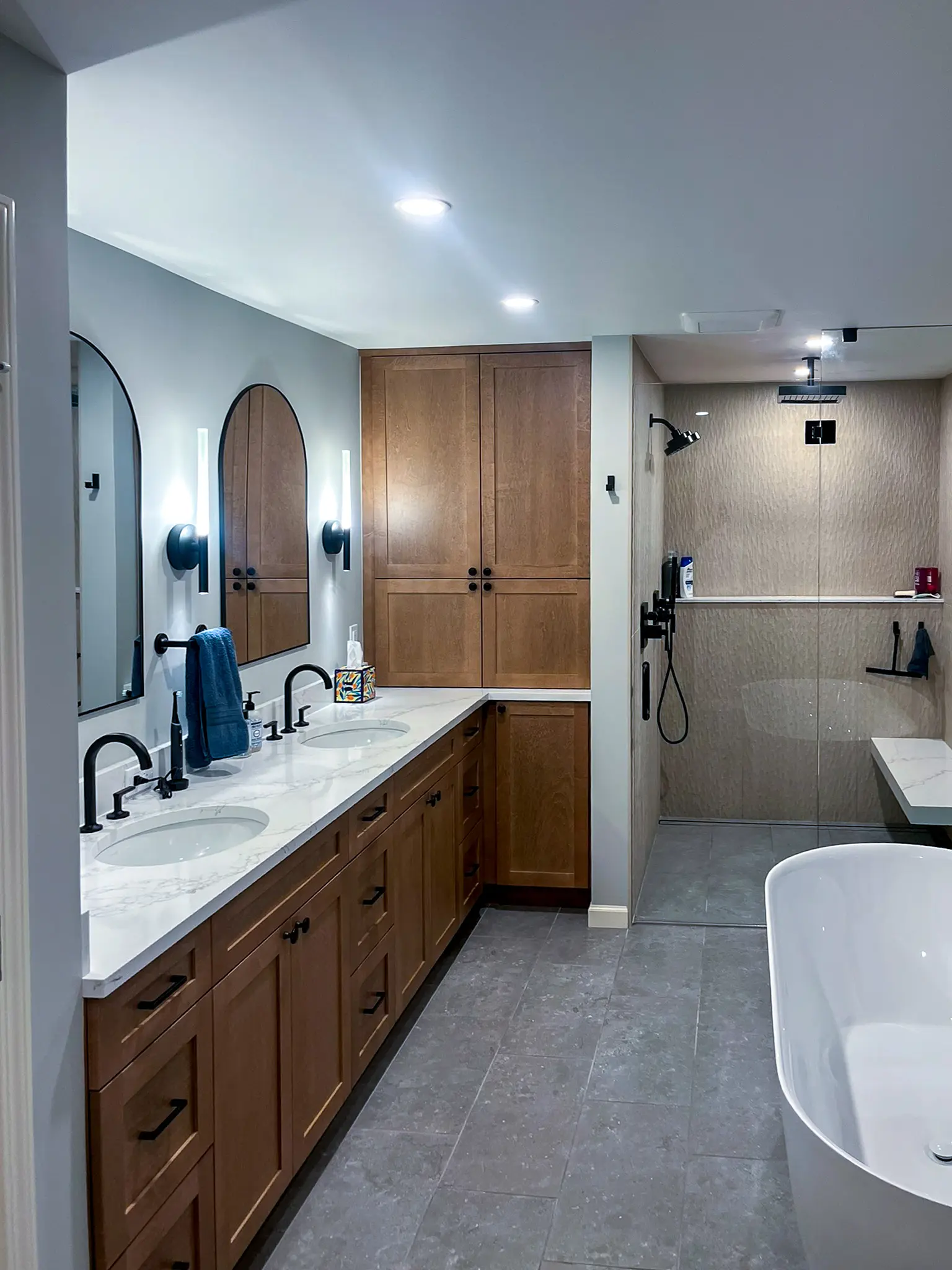 Primary bathroom double vanity with wood cabinetry, black fixtures, and a view into the curbless tiled shower in a Bellevue, WA home.