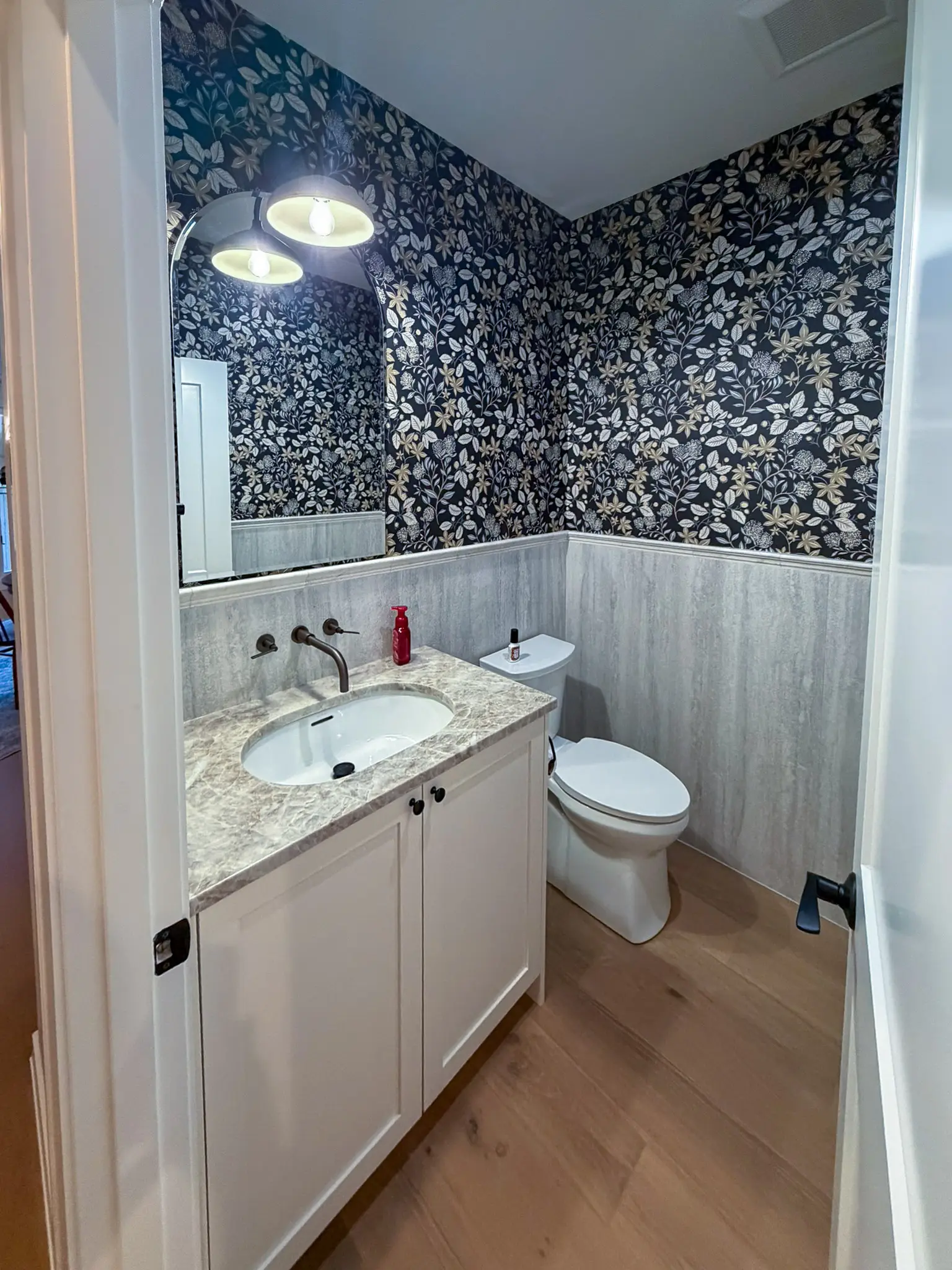 Powder room with floral wallpaper, an arched mirror, and a white vanity after a whole-home remodel in Sammamish, WA.