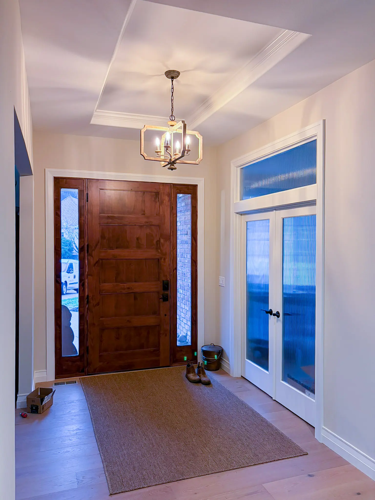 Entryway with a wood front door, tray ceiling, and pendant chandelier after a whole-home remodel in Sammamish, WA.
