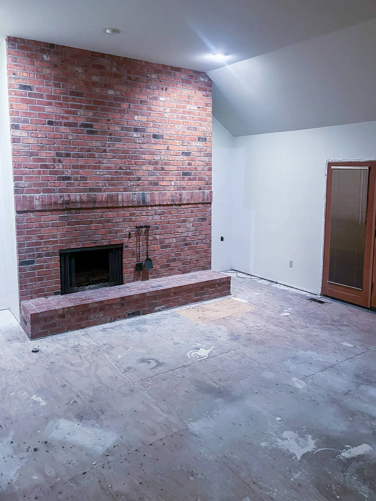 Living room with an exposed brick fireplace and plywood subfloor before a whole-home remodel in Sammamish, WA.