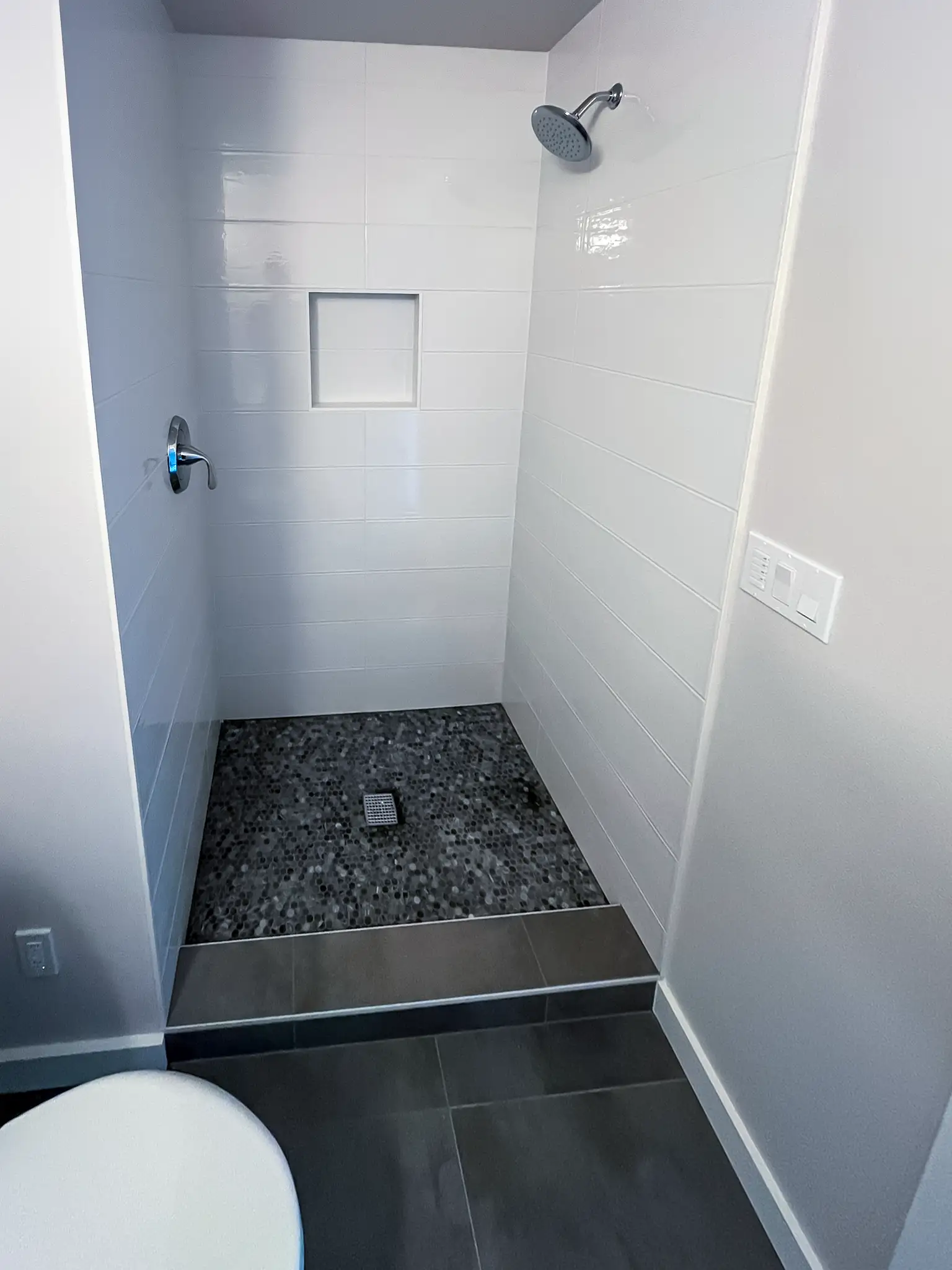 Curbless tiled shower with a pebble floor and rain shower head in a remodeled Kirkland, WA bathroom.