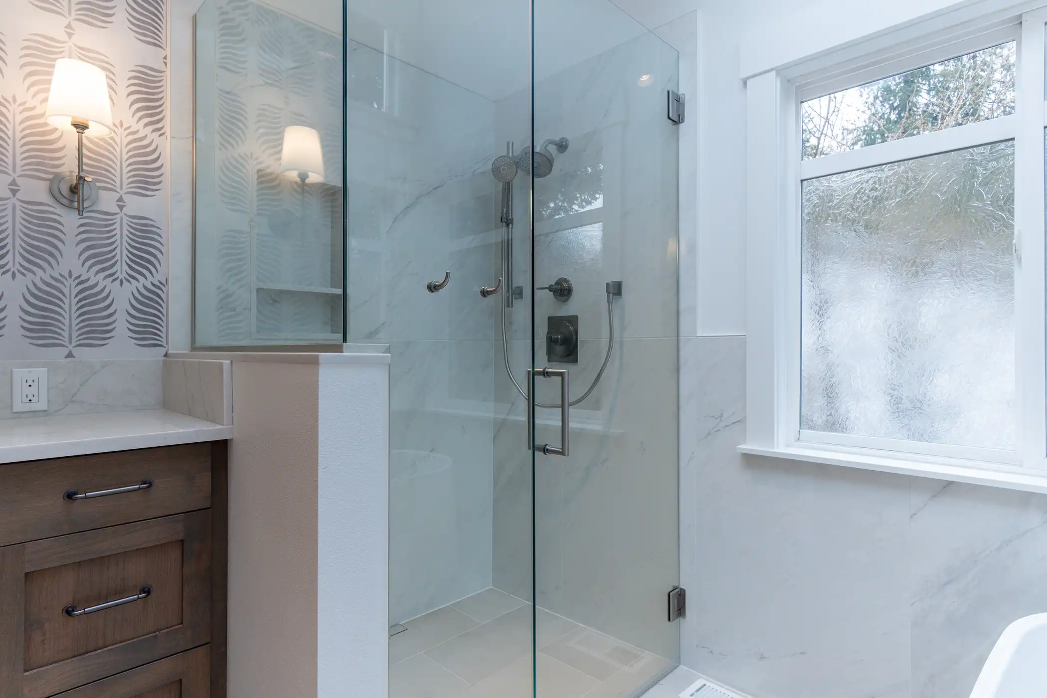 Glass-enclosed shower with marble-style tile in the remodeled bathroom of a Kirkland, WA home.