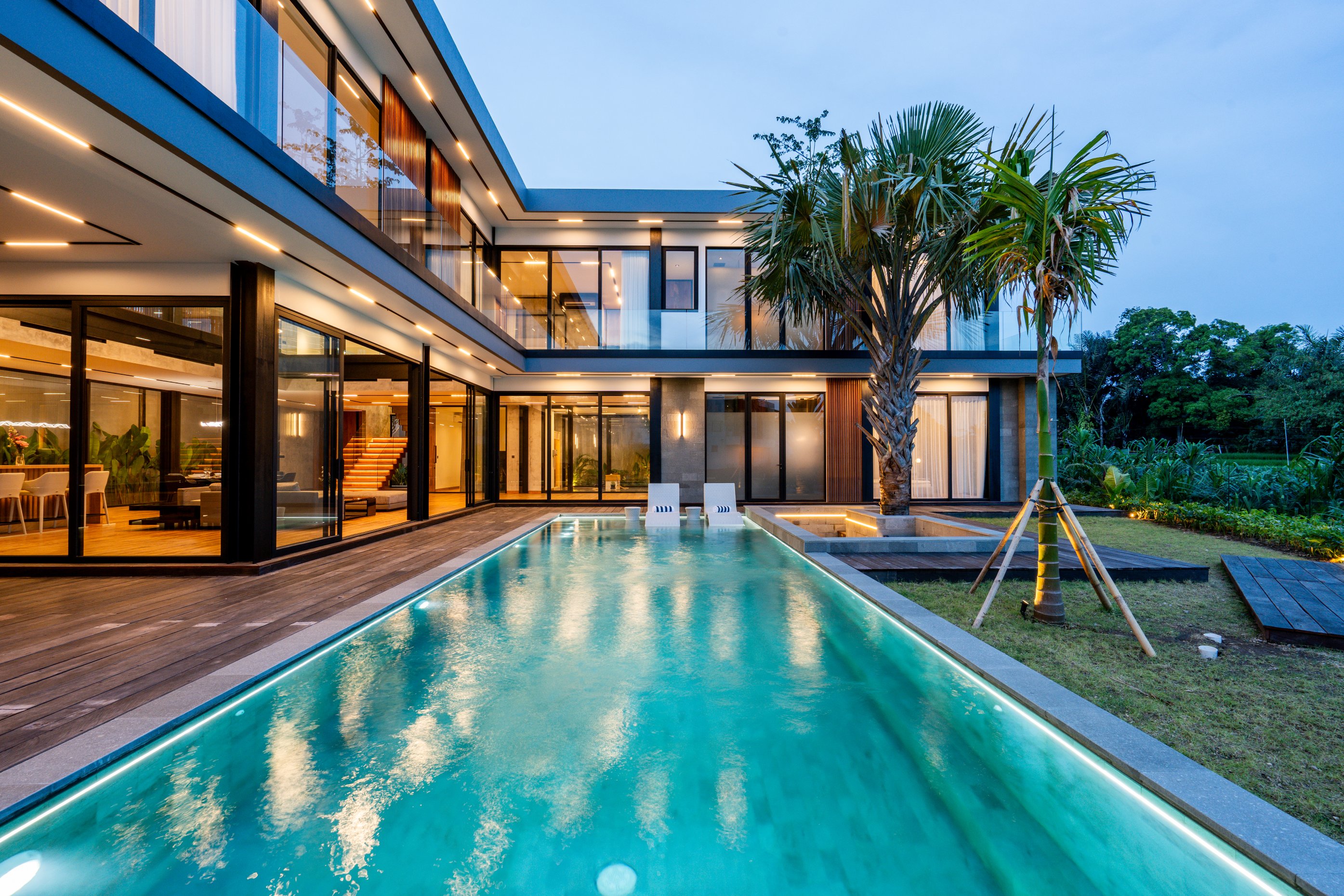 Modern two-story house with large glass windows and a pool featuring a pink flamingo float at dusk.