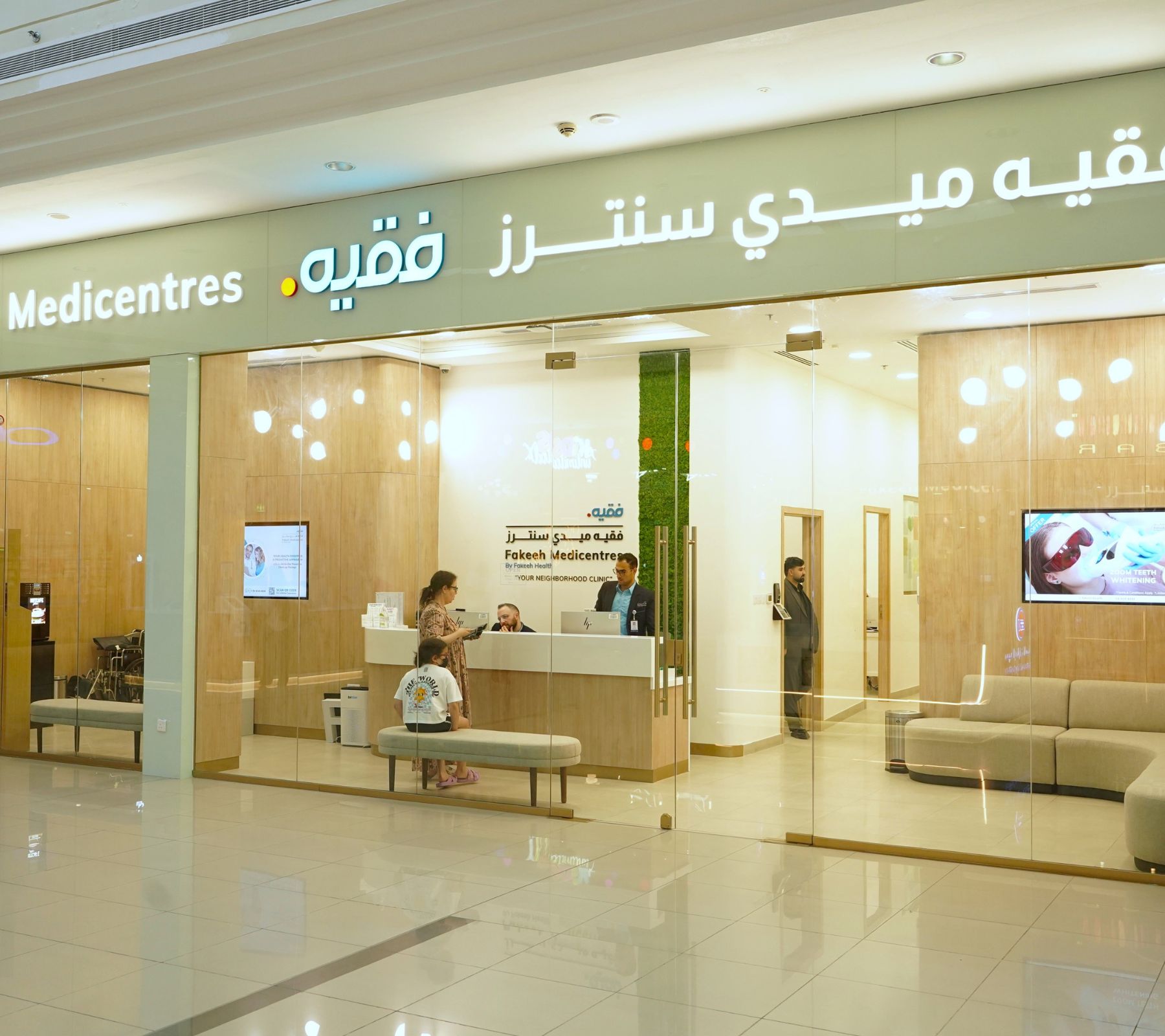 Entrance of Fakieh Medicentres clinic with reception desk and staff attending to visitors behind glass walls.