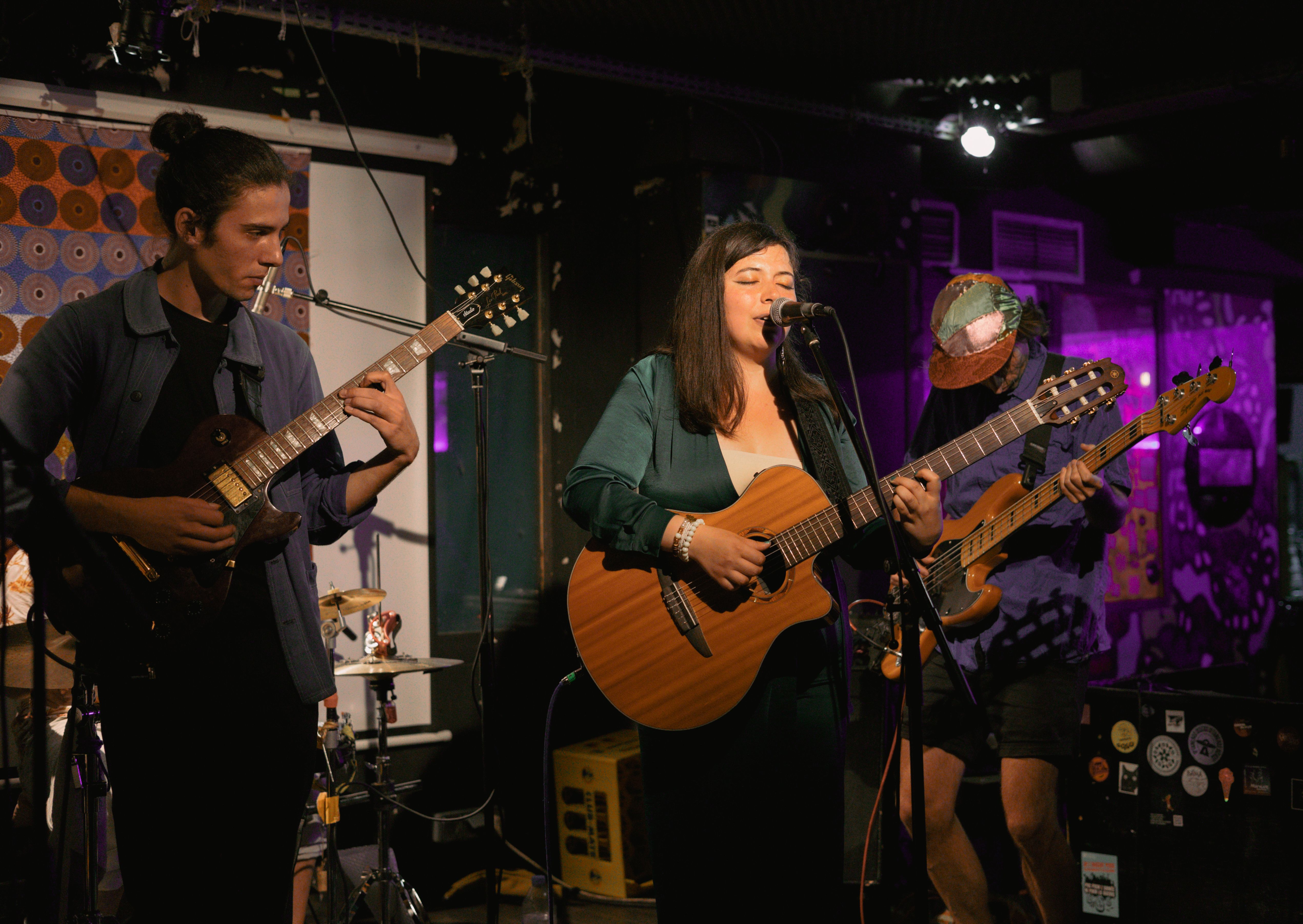 Groupe de musique avec une chanteuse et deux guitaristes jouant sur scène dans un club.
