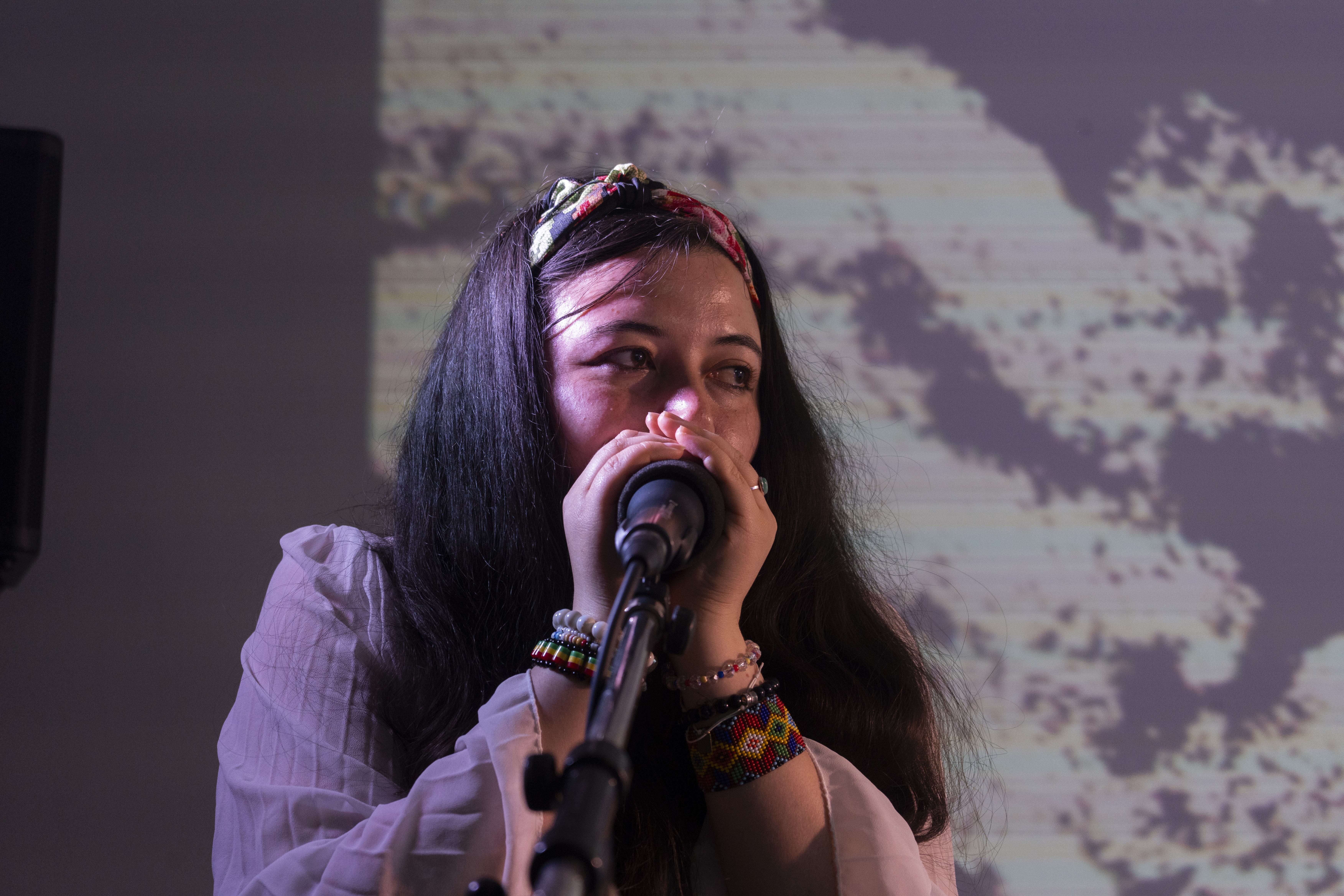 Femme chantant dans un micro avec bracelets colorés et fond flou à motifs.