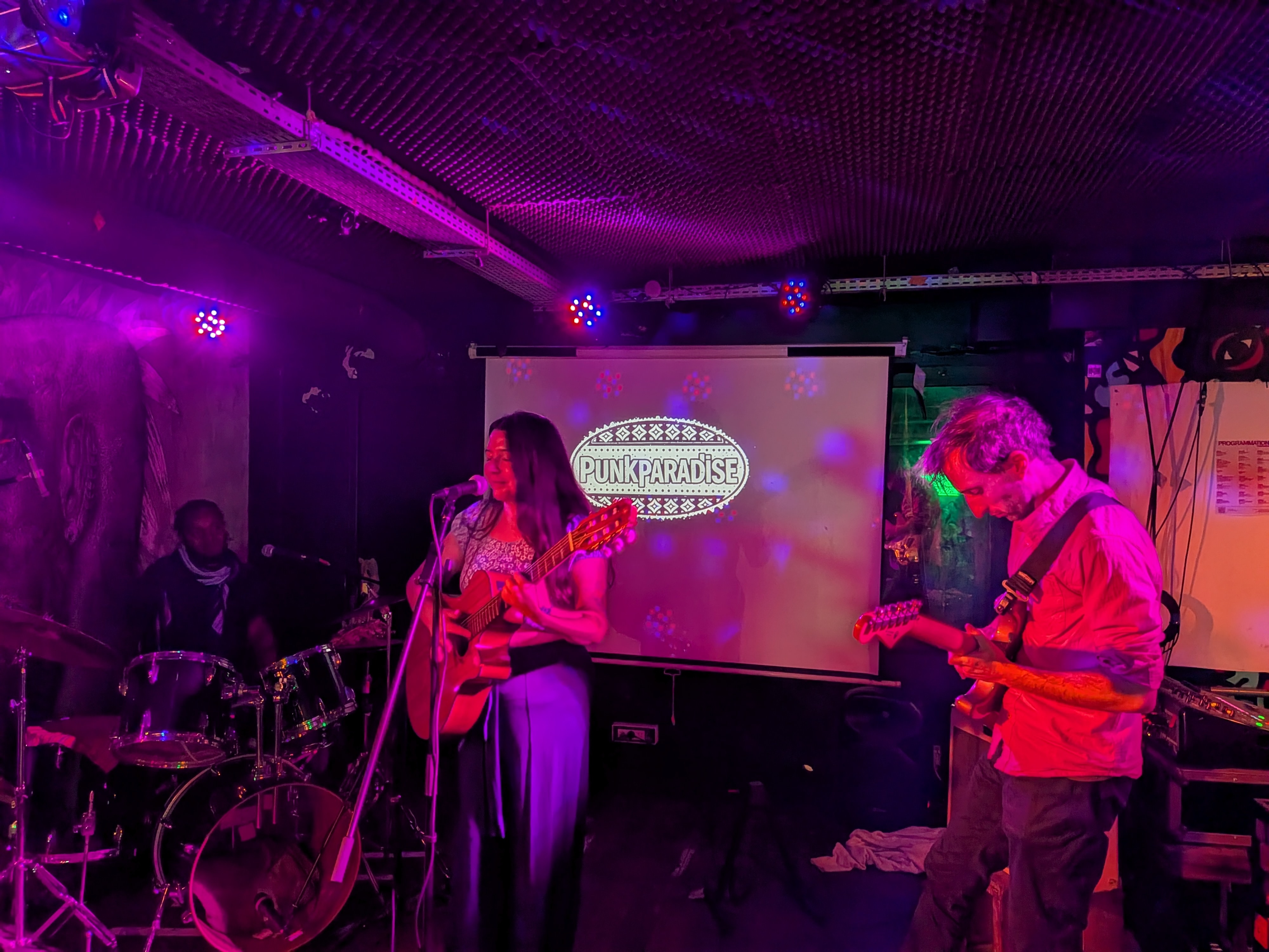 Groupe musical en concert avec chanteuse à la guitare acoustique, guitariste électrique et batteur dans club.