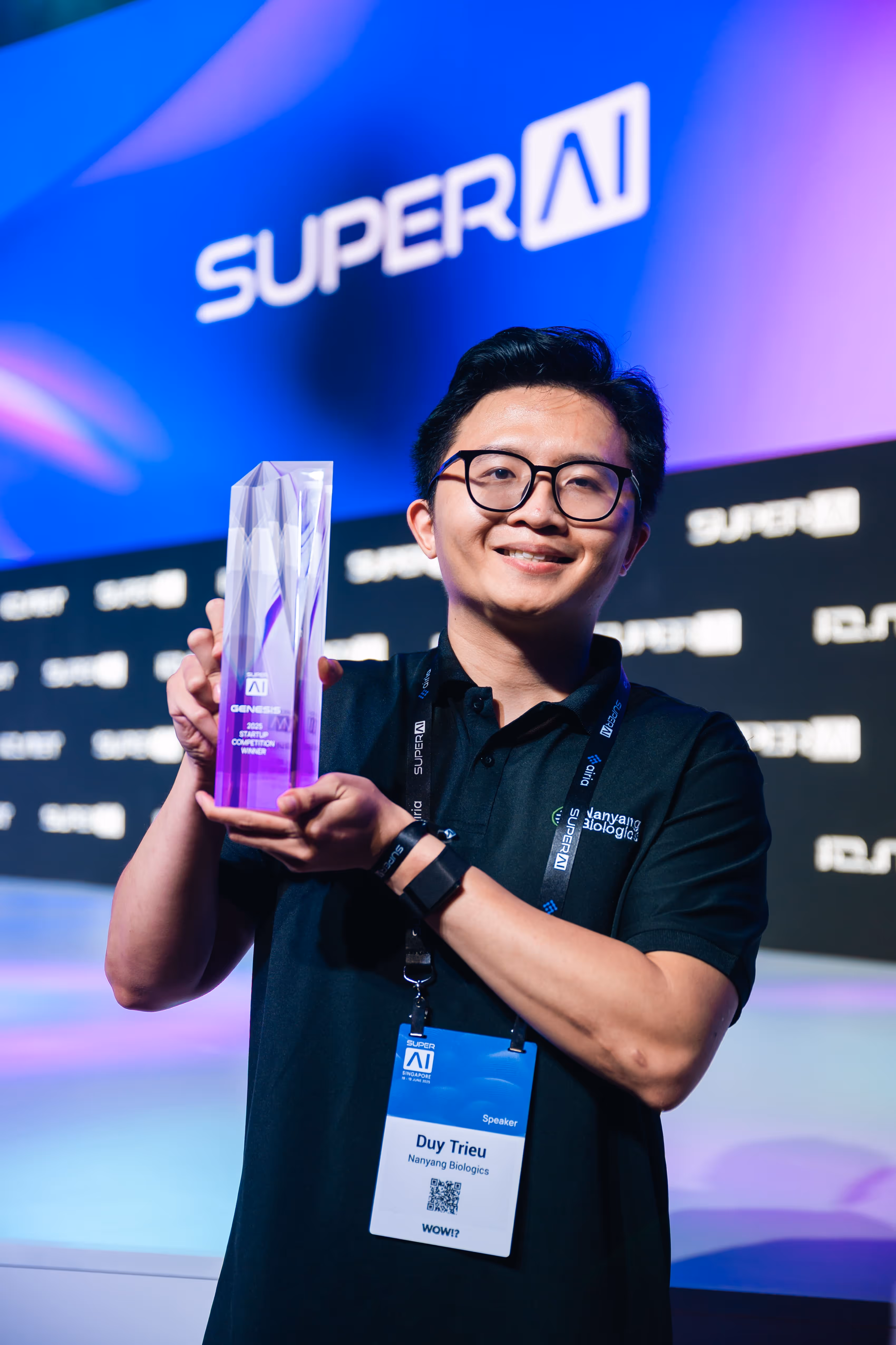 Man wearing glasses holds a transparent trophy at SuperAI event with a stage backdrop.