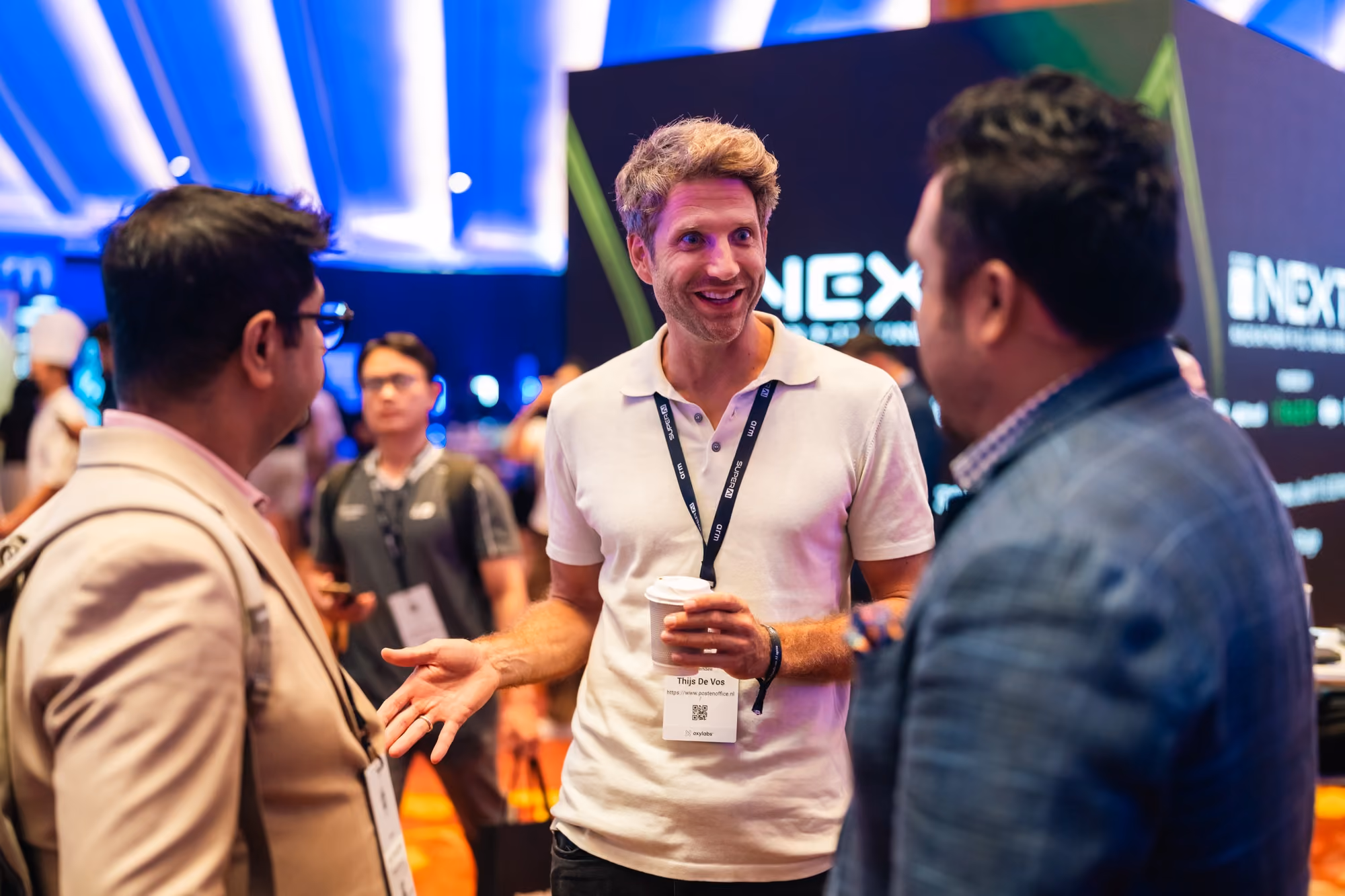 Attendee wearing a "Thijs De Vos" badge chatting with two others near the NEXT stage at SuperAI 2026.