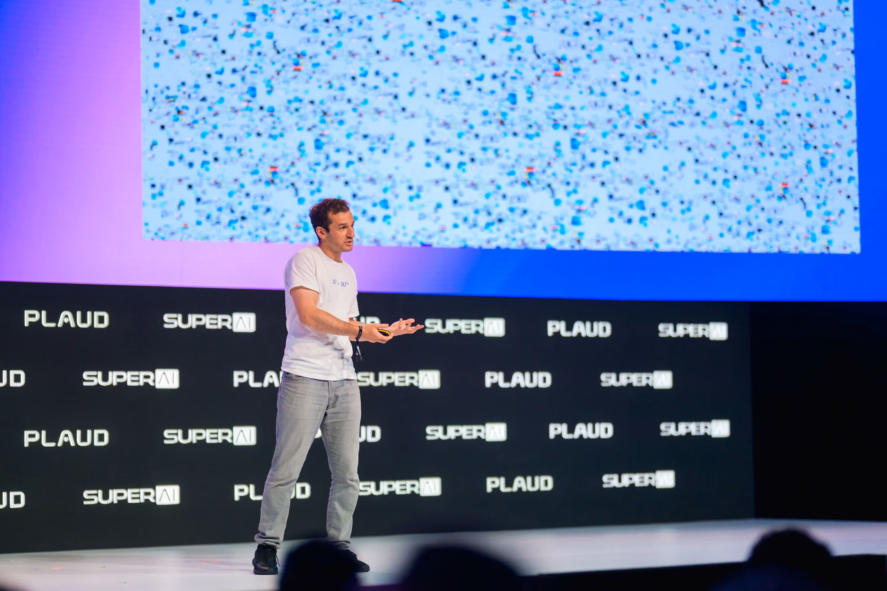 Will Bryk, Exa CEO, speaking on the SuperAI main stage with a data visualization displayed behind him.
