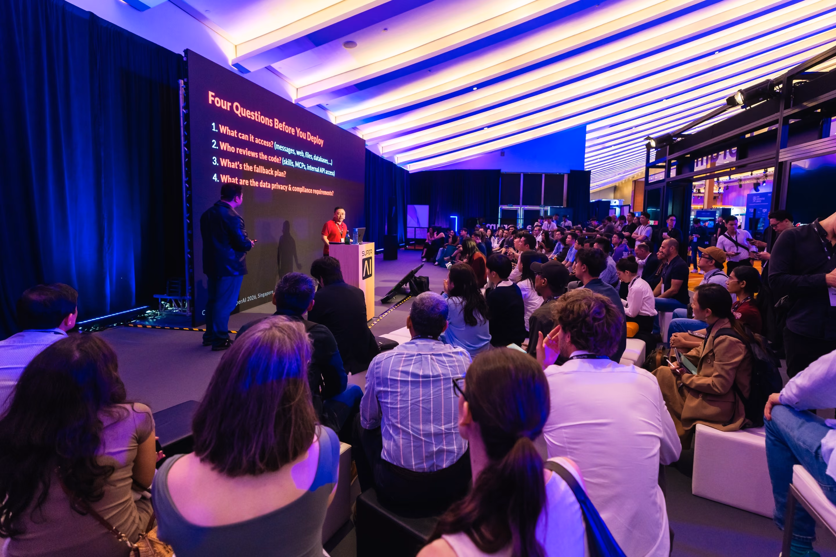 Speaker presenting "Four Questions Before You Deploy" to a seated audience at SuperAI 2026.