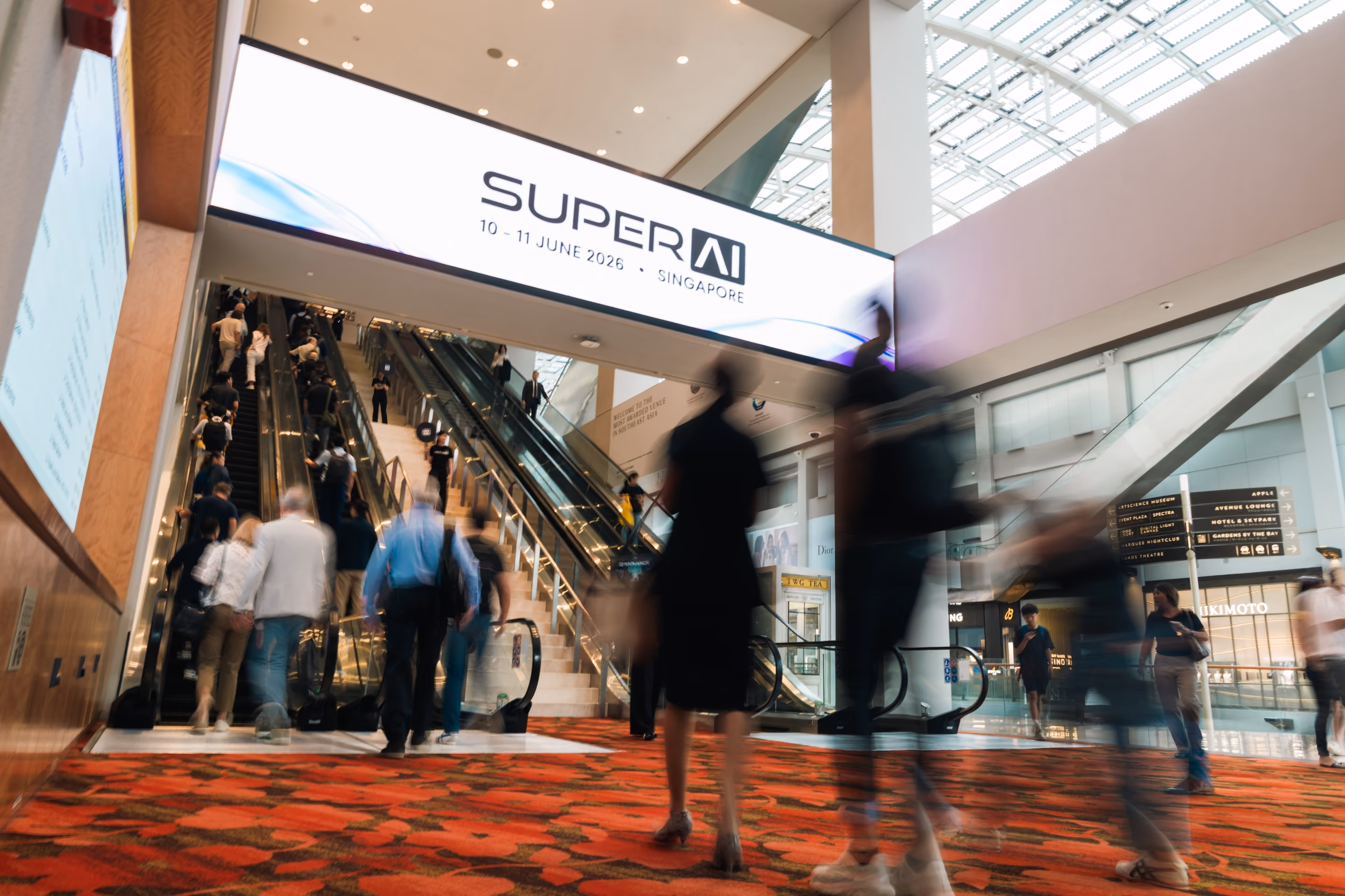 Attendees walking up an escalator beneath a "SUPER AI 10–11 June 2026, Singapore" sign at the venue entrance.