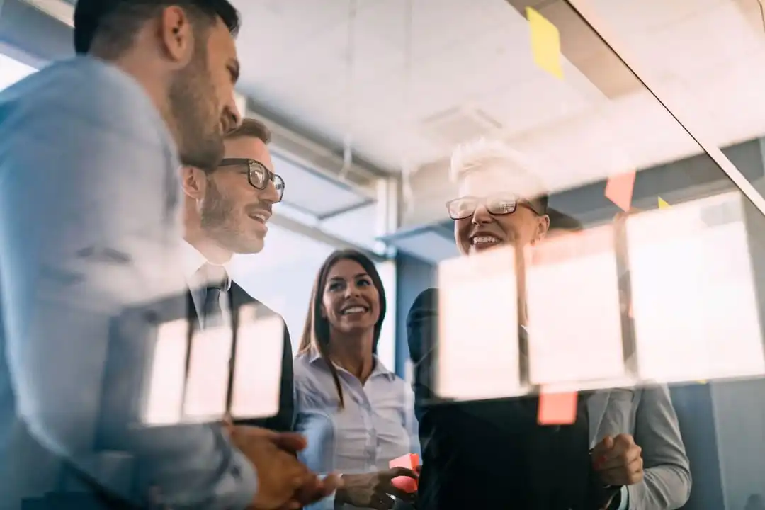 Men and women dressed in business attire talking in meeting room surrounded by glass