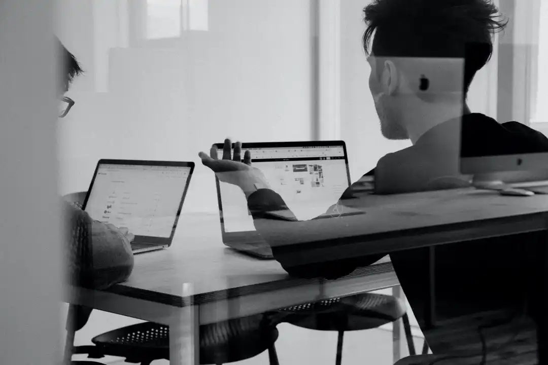 Two people working at table with laptops in conference room