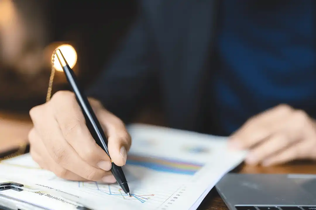 Woman writing on paper with graph chart on desk