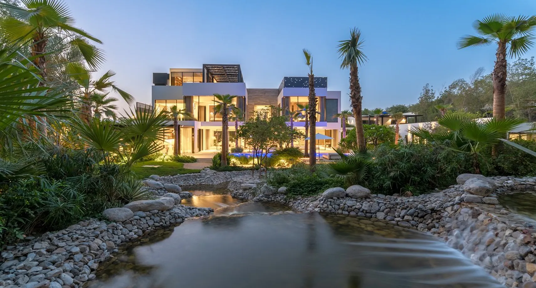 Modern luxury villa with warm lighting and a flowing stream in the garden
