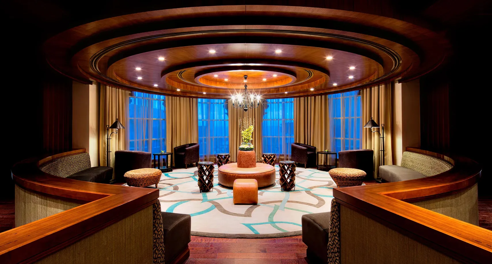 Contemporary hotel lounge interior design featuring rich wood finishes, circular seating arrangement, and chandelier lighting
