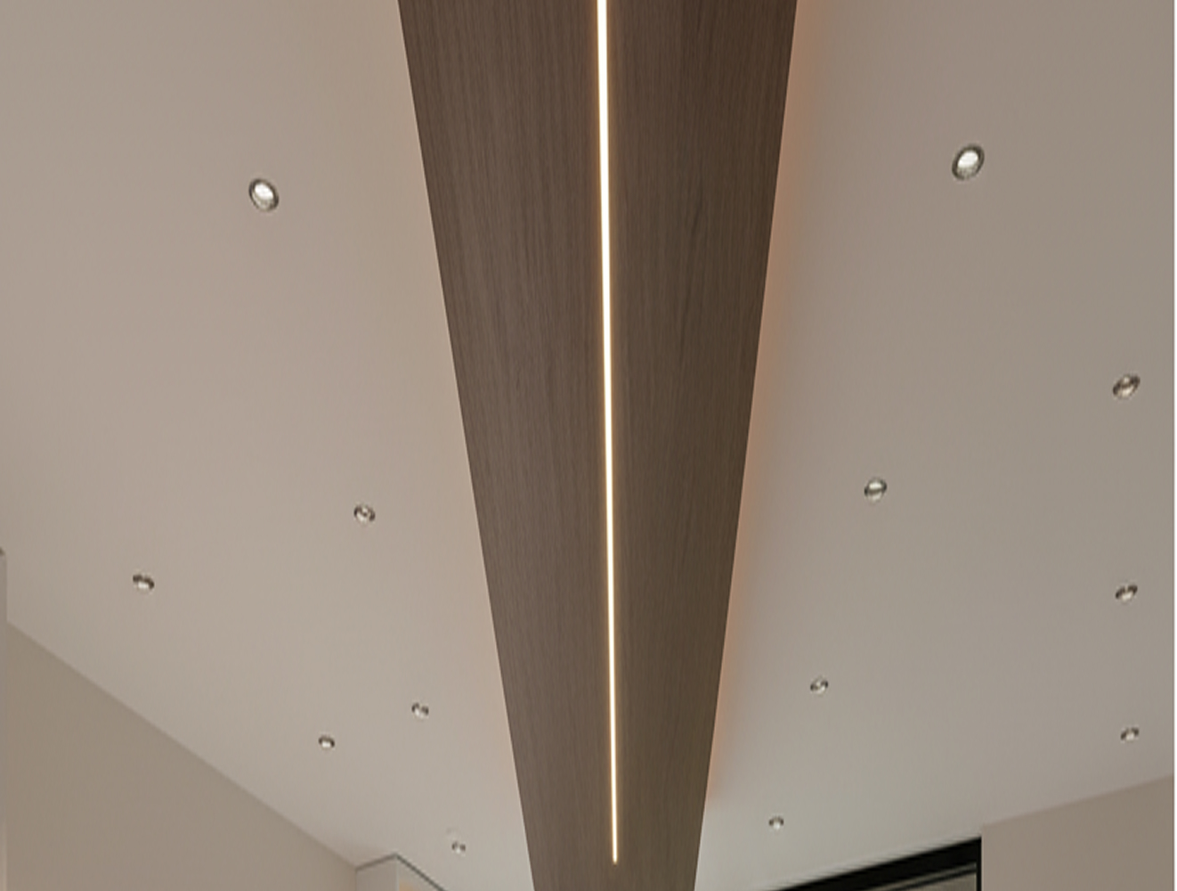 Interior ceiling design featuring a linear wooden panel surrounded by recessed spotlights.