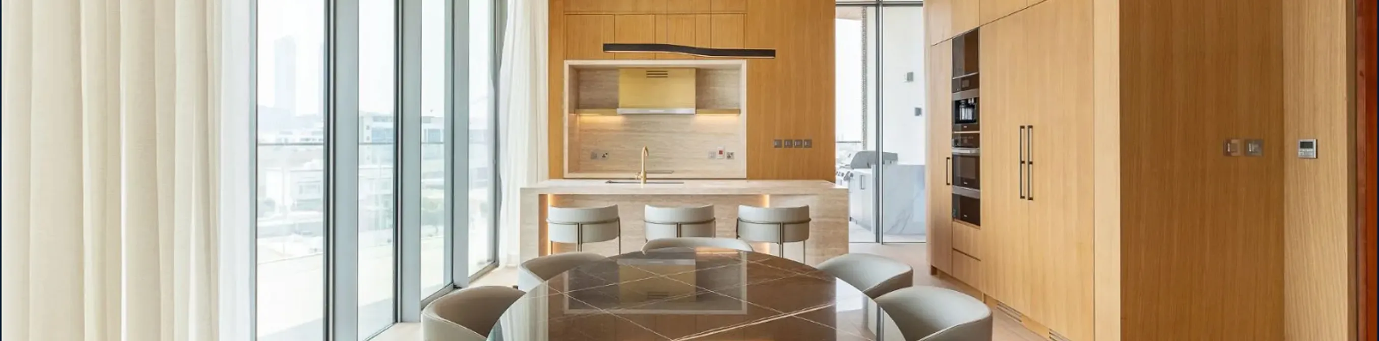 Modern open-plan kitchen and dining with wood cabinetry, an island, and expansive windows.