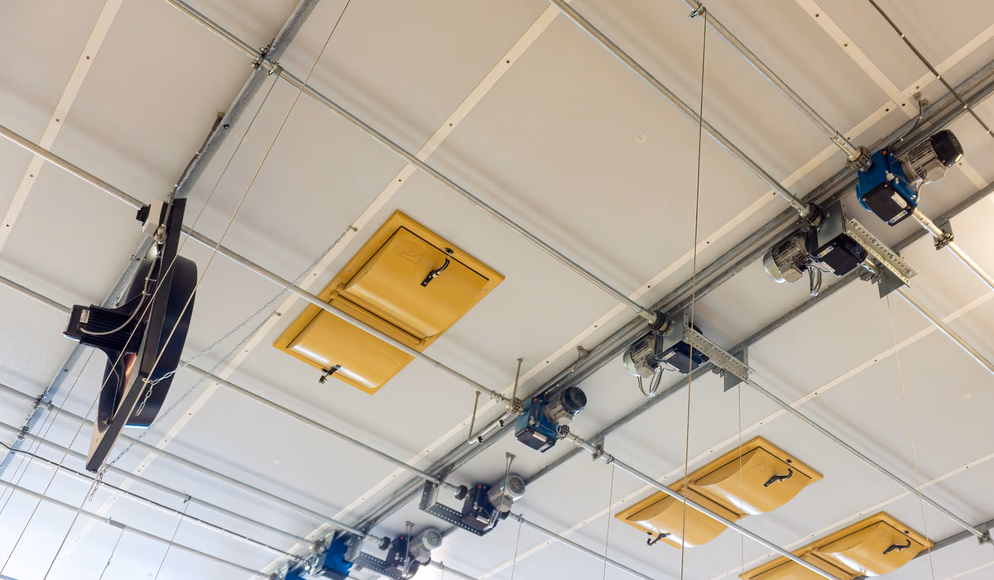 Industrieel plafond met gele ventilatieluiken, motoren en een metalen buizenframe.