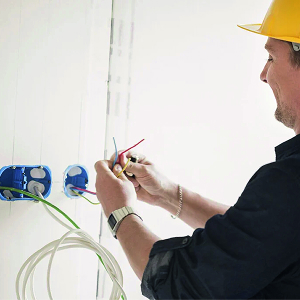 Électricien portant un casque de sécurité jaune travaillant sur une installation électrique murale avec des câbles colorés