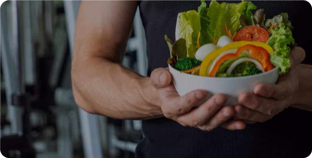 Person in black shirt holding a bowl of fresh salad with lettuce, tomato, peppers, and broccoli.