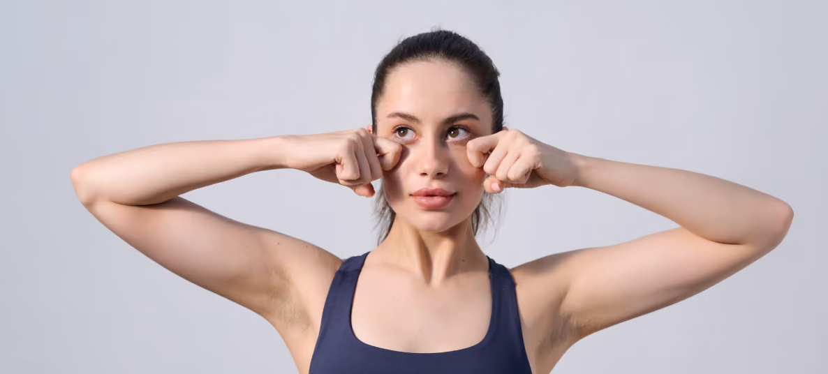 Woman in navy tank top pressing her fingers against under-eye skin in a face exercise.