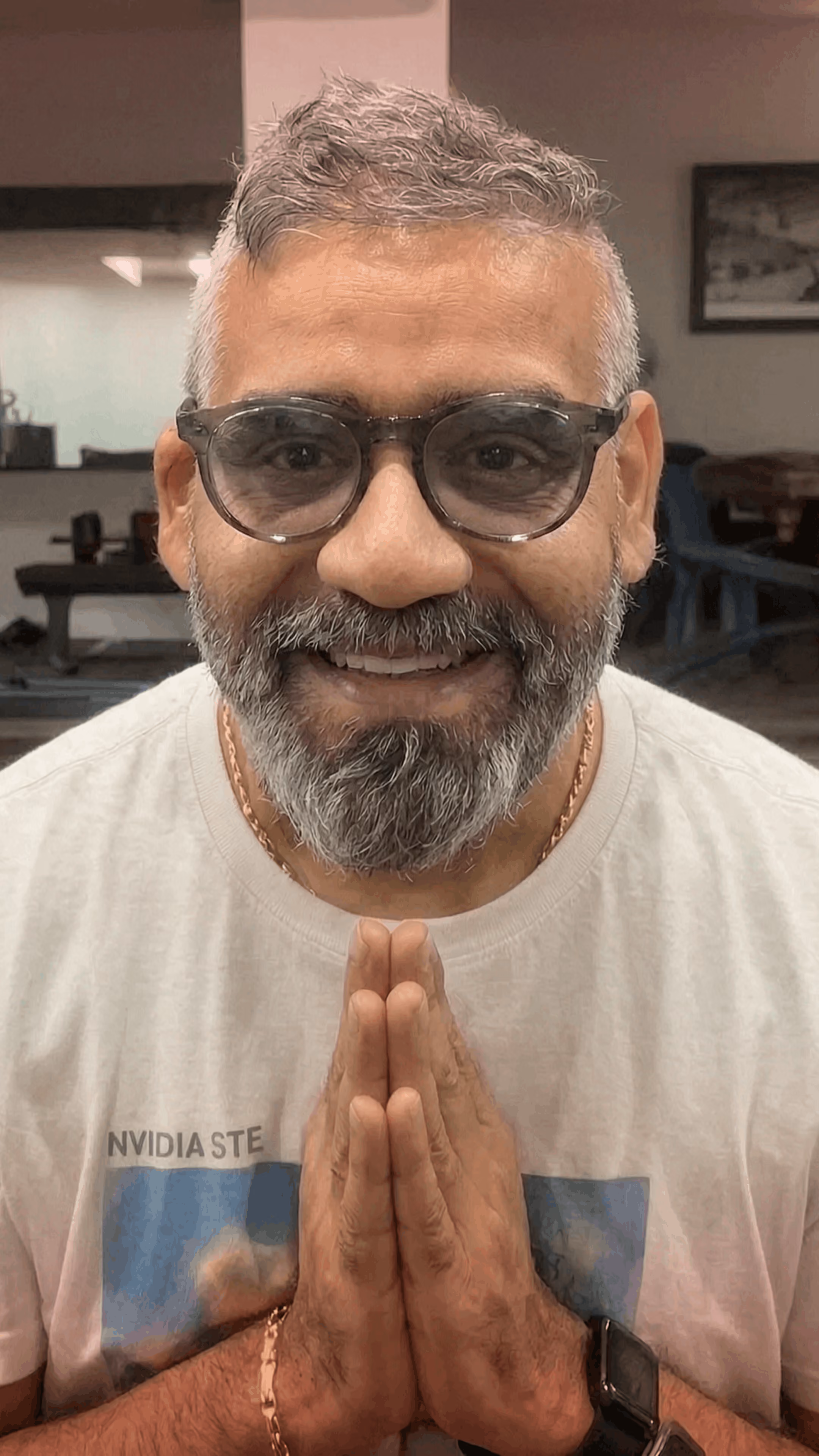 Smiling man with glasses wearing a blue shirt in a softly lit indoor setting.