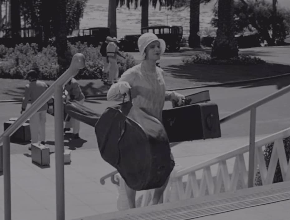 Дафна поднимается по лестнице с чемоданами