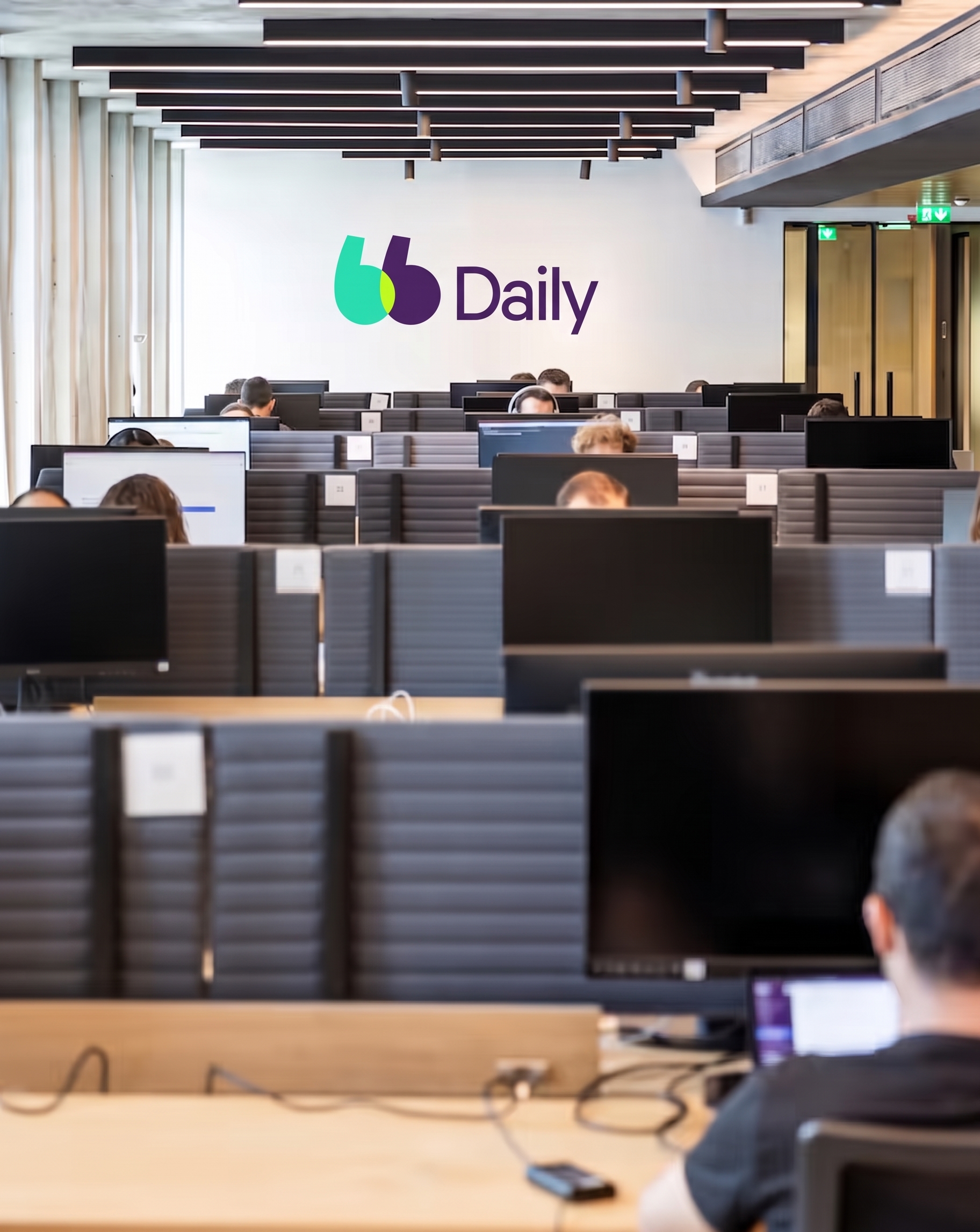 Logo de BlaBlaCar Daily sur un mur au fond d'une salle rempli de collaborateurs sur leur ordinateur