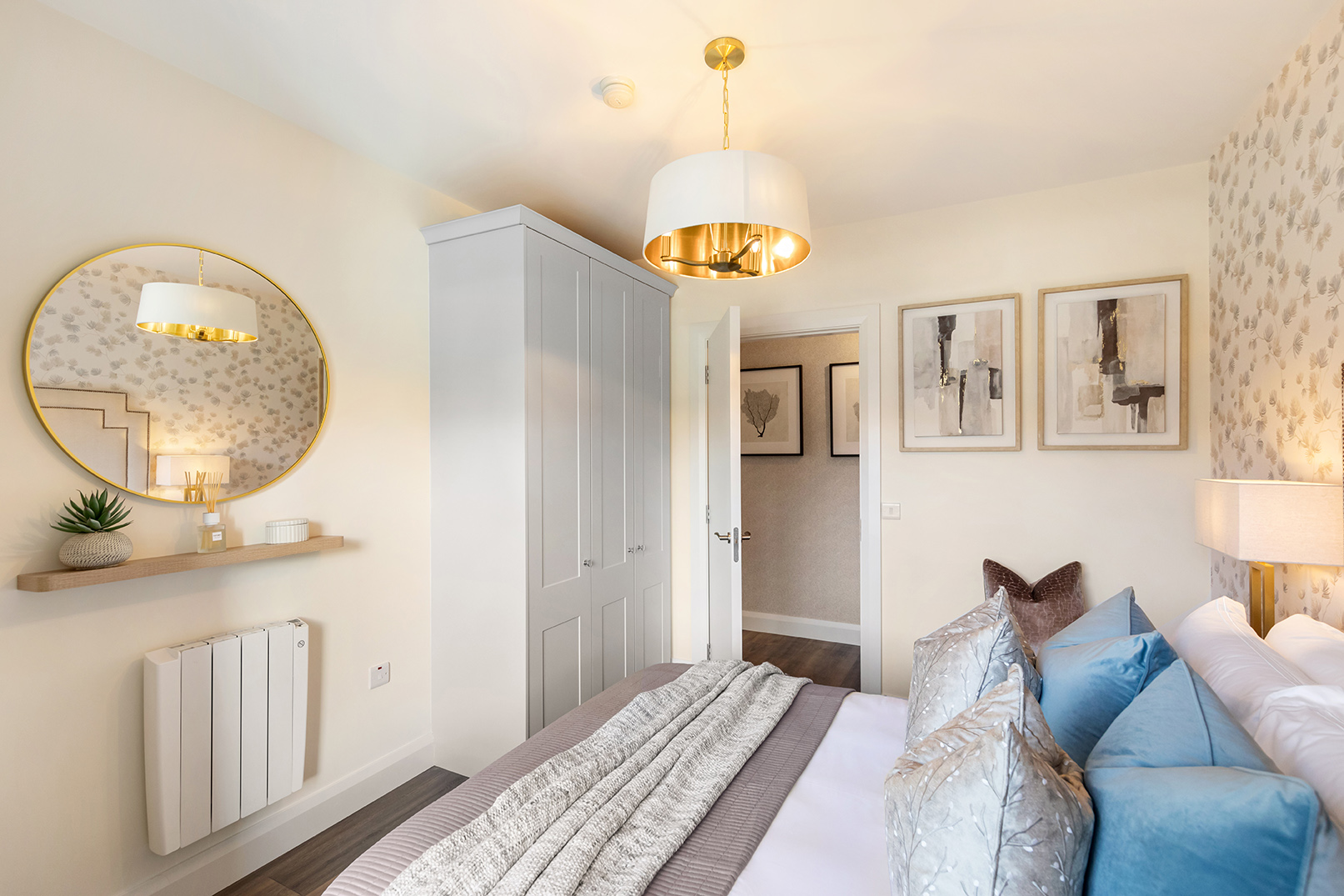 Cozy bedroom with a bed featuring multiple pillows and blankets, a wardrobe, round wall mirror, and warm lighting.