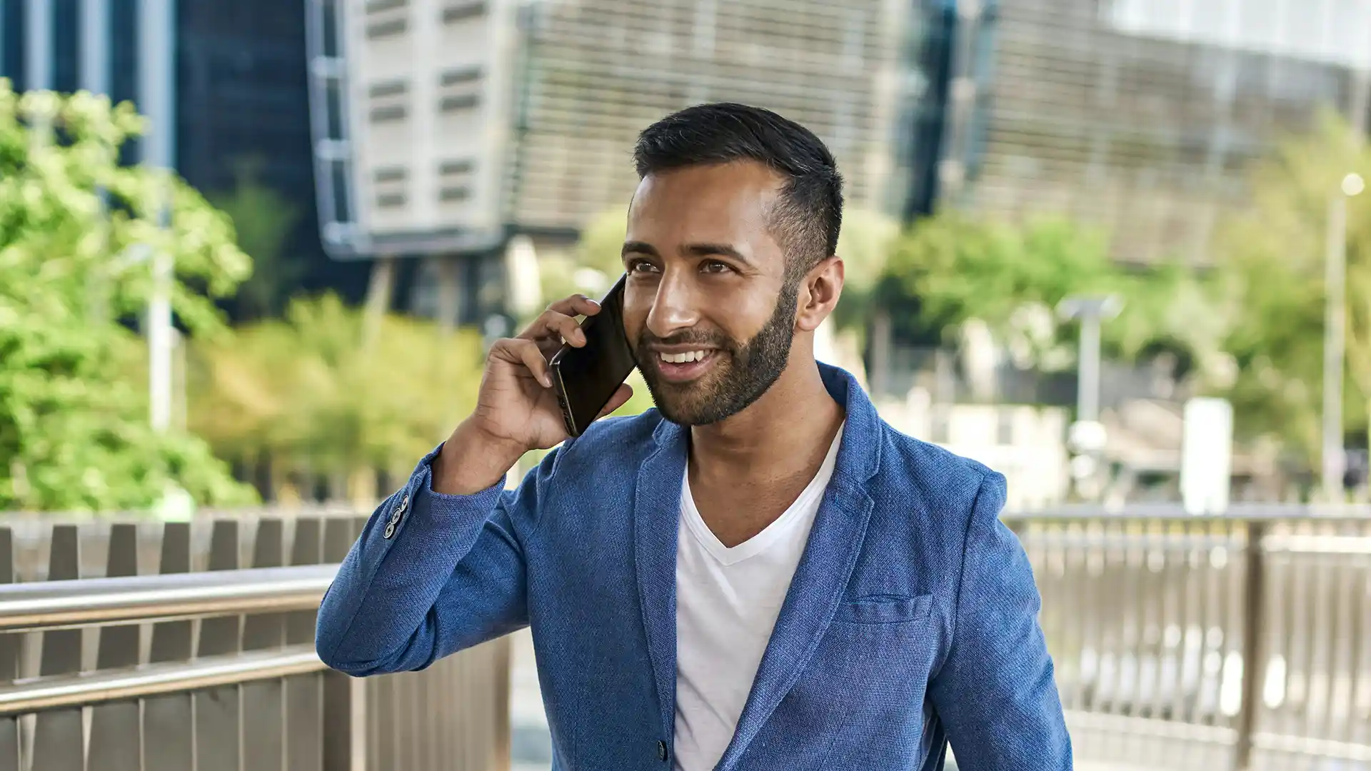 Indian man smiling while talking on the phone outdoors in Dubai, representing professionals moving to Dubai from India for career growth