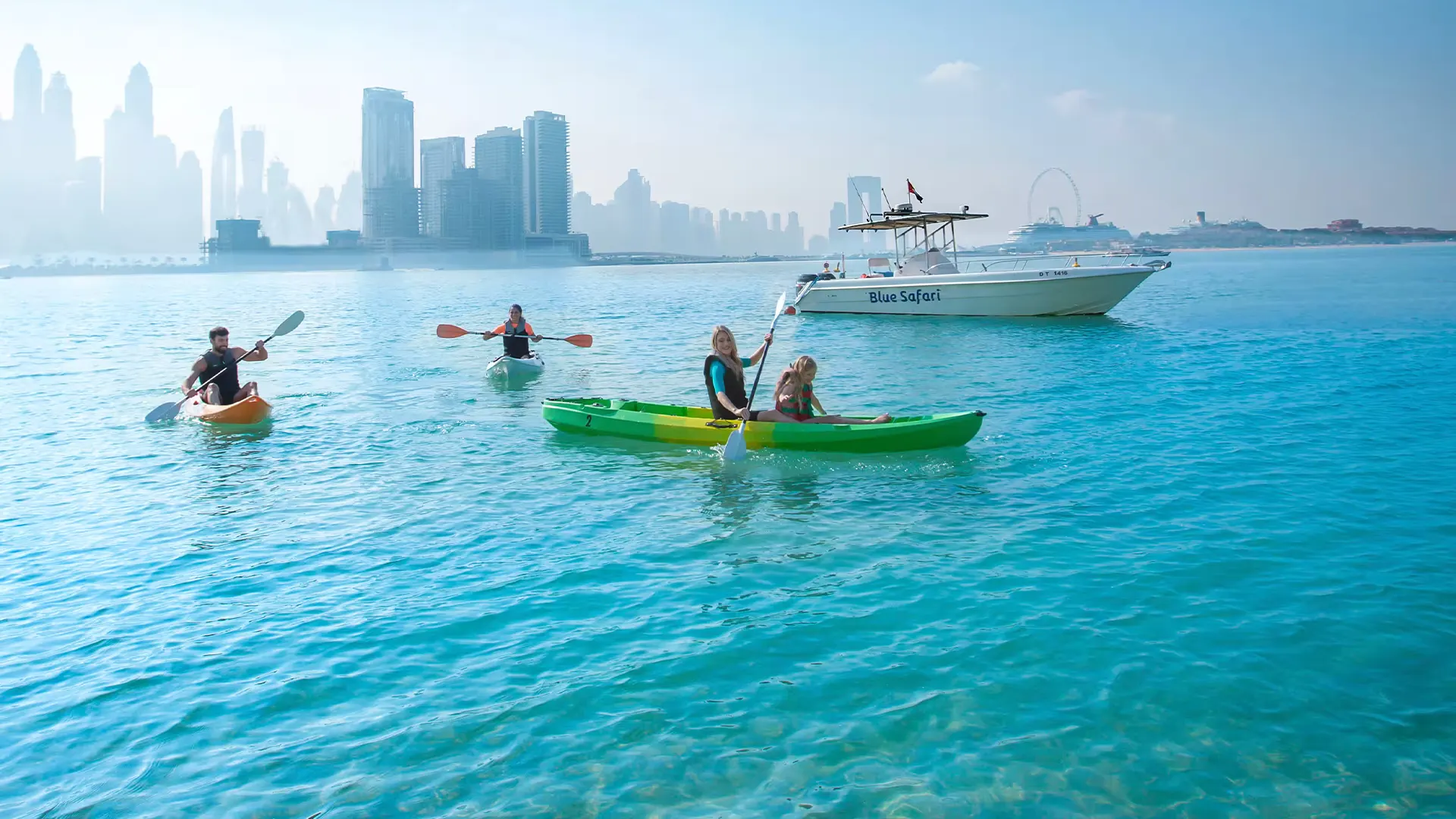 Clear blue skies and calm waters under sunny Dubai weather, with people kayaking and a boat near the city skyline.