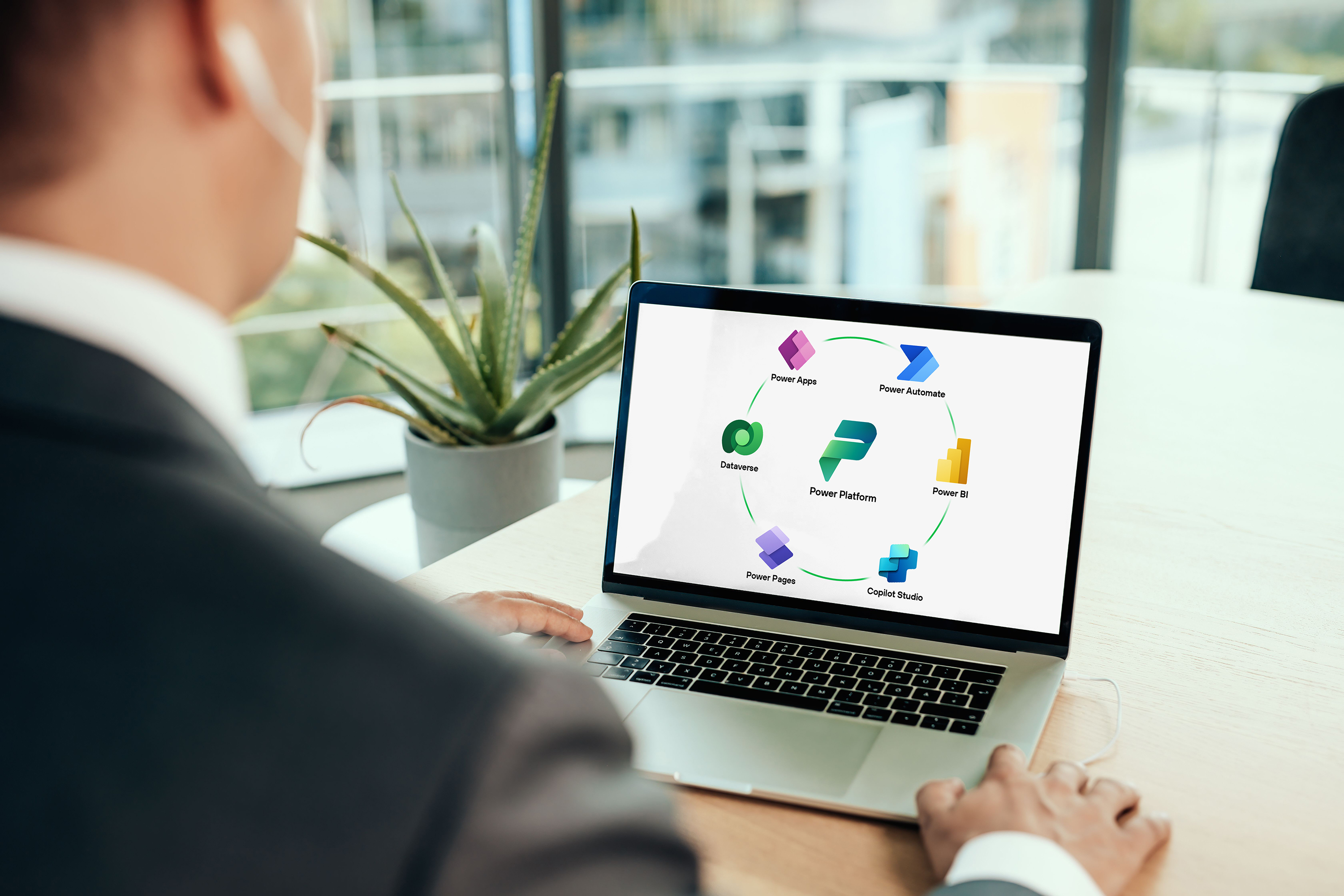 A person in a suit using Microsoft Power Platform on a laptop screen in a bright office setting, with a plant visible in the background.