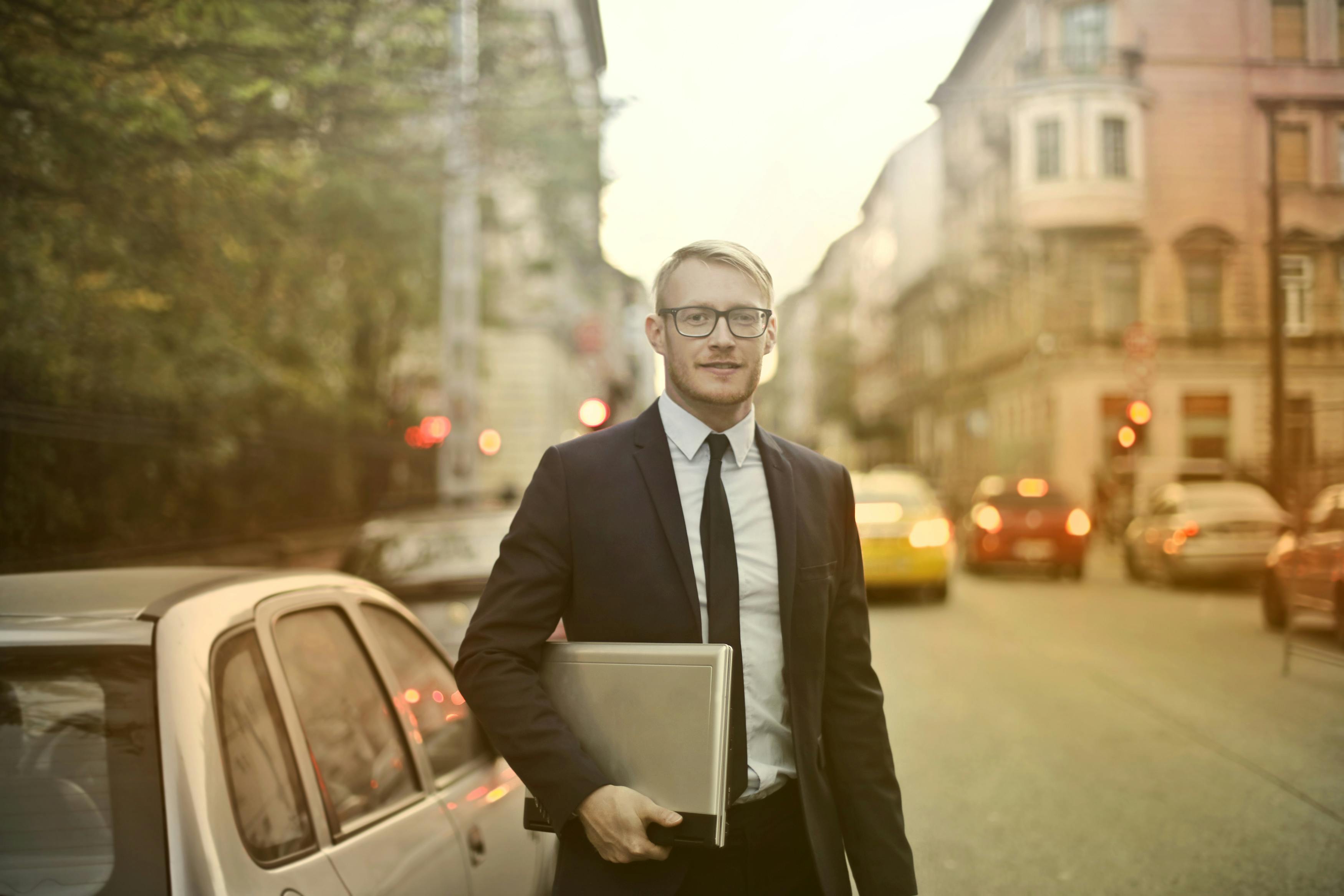 Smartly dressed solar panel sales representative holding a laptop, standing on a city street during sunset