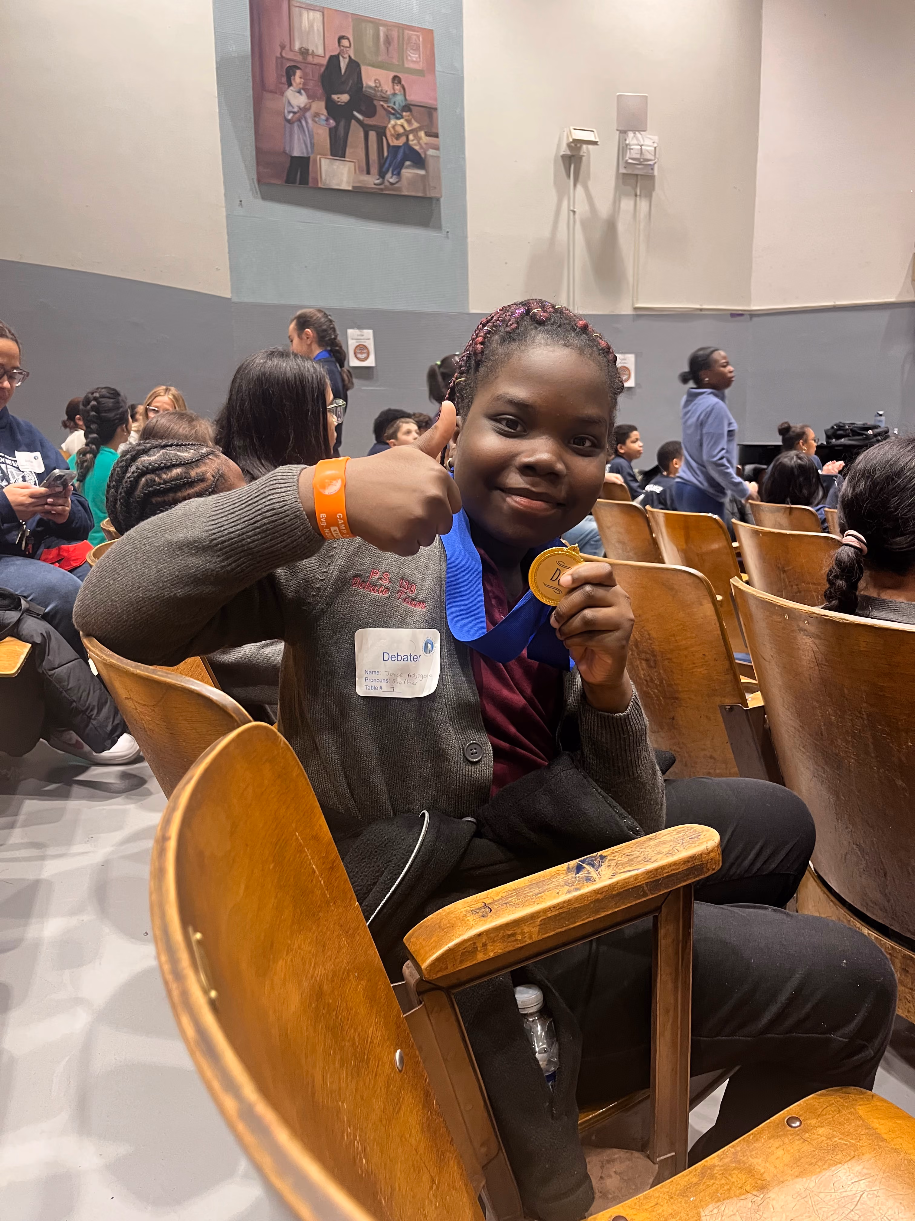 Student debater holds gold medal and gives thumbs up at competition
