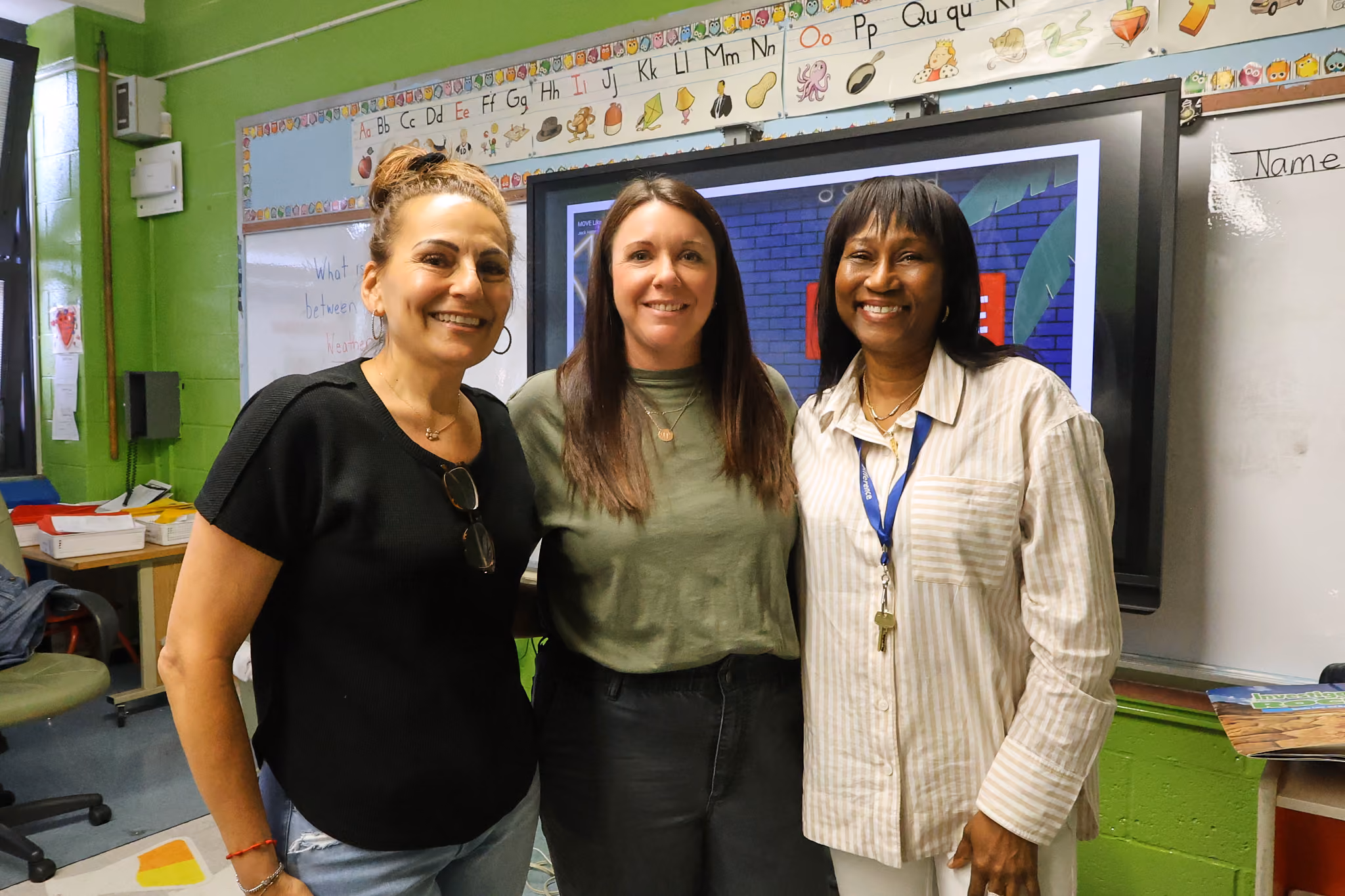 Three smiling staff members pose together in a decorated elementary classroom