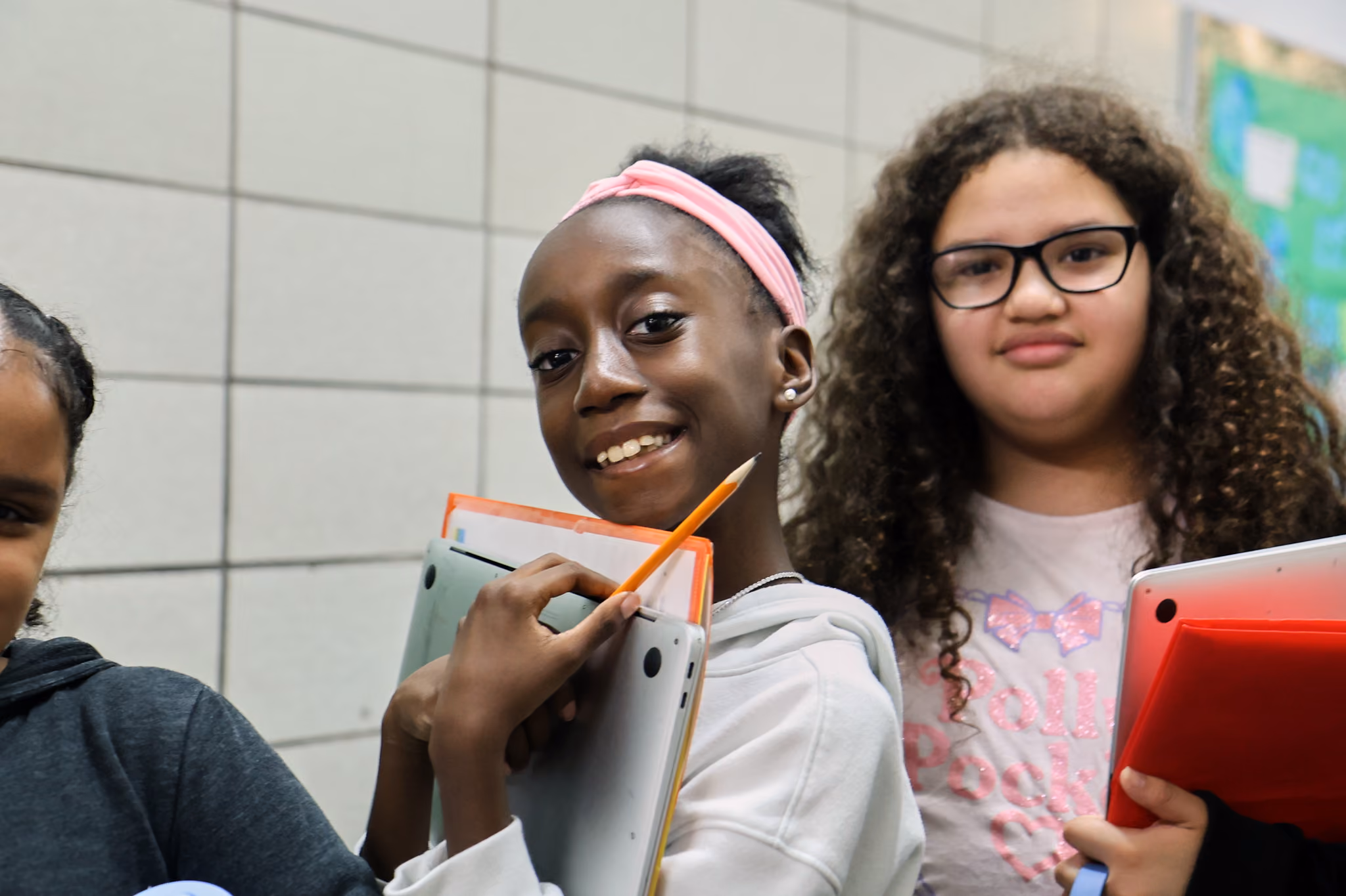 Two middle school students smiling and holding laptops and school supplies