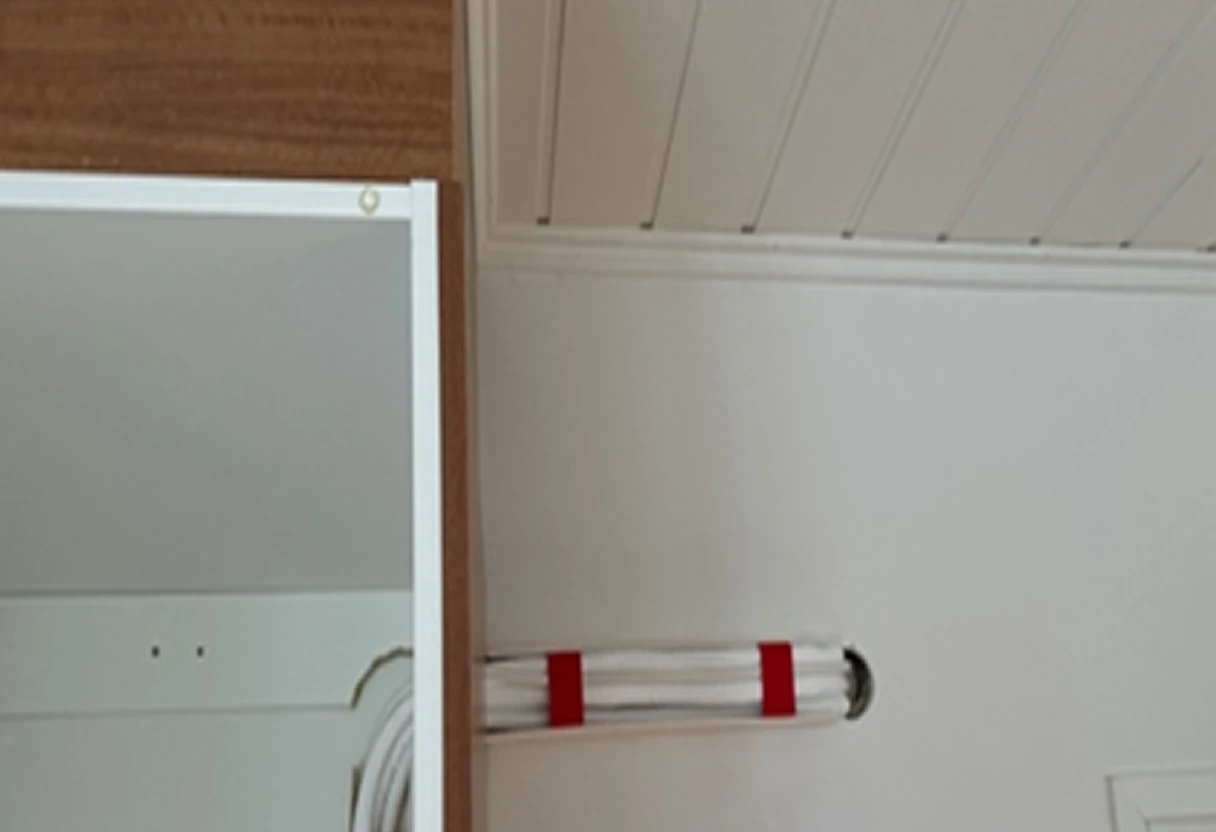 Sisäinen seinä, jossa on valkoinen putkikimppu kiinnitettynä punaisilla nippusiteillä reikäaukosta toiseen.