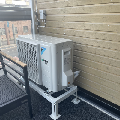 Daikin-lämpöpumpun valkoinen ulkoyksikkö puuverhoillun rakennuksen seinustalla